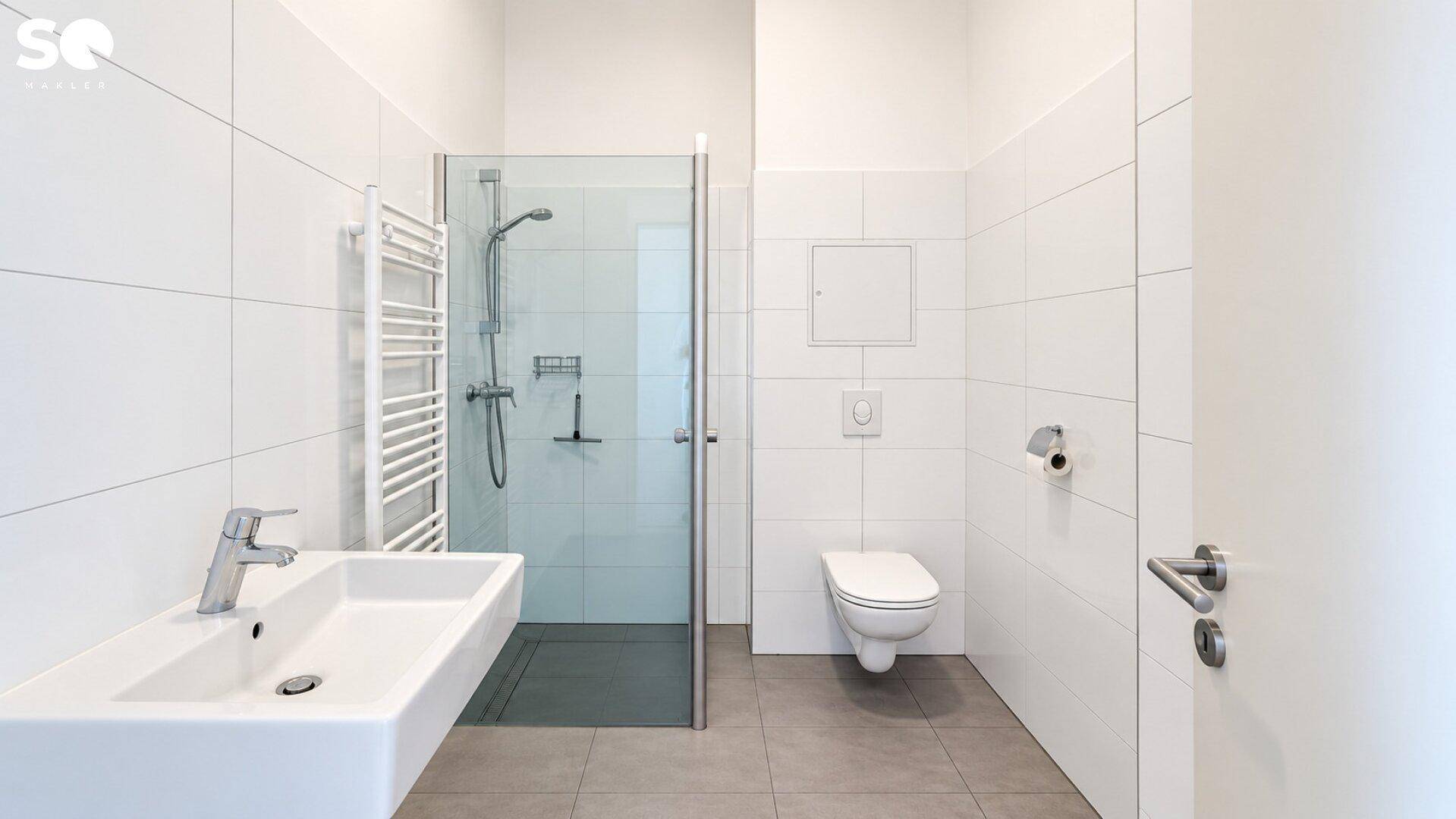 Modernes Badezimmer mit weißen Fliesen, ebenerdiger Dusche und wandhängendem WC.