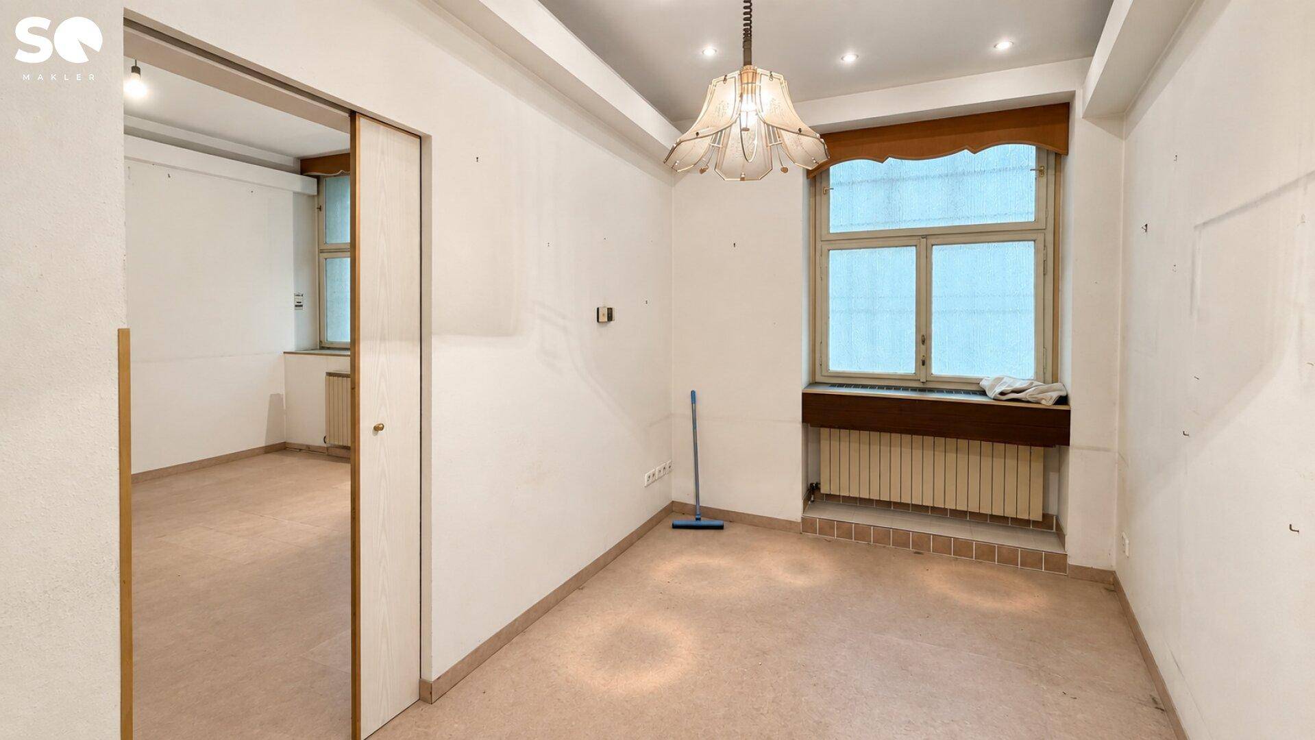 Weiterer leerer Raum mit einem Fenster, Heizkörper und einer dekorativen Deckenlampe.