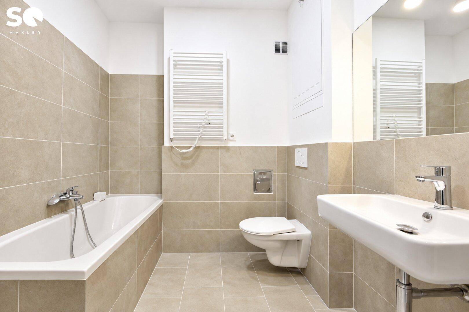 Modernes Badezimmer mit Badewanne, Wand-WC, Einzelwaschbecken und beigen Fliesen.