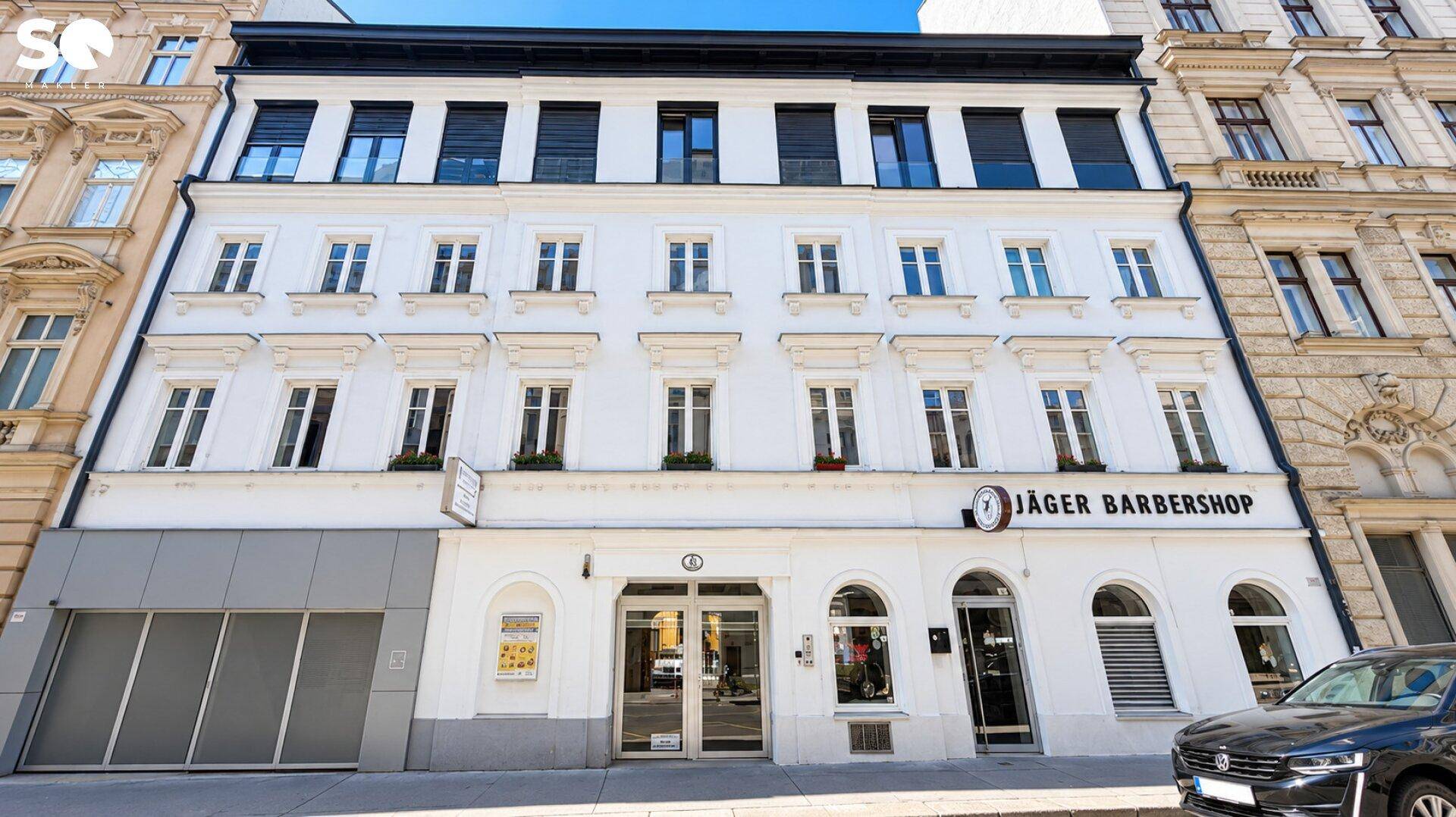 Klassische weiße Fassade eines Mehrfamilienhauses mit vielen Fenstern und Geschäften im Erdgeschoss.