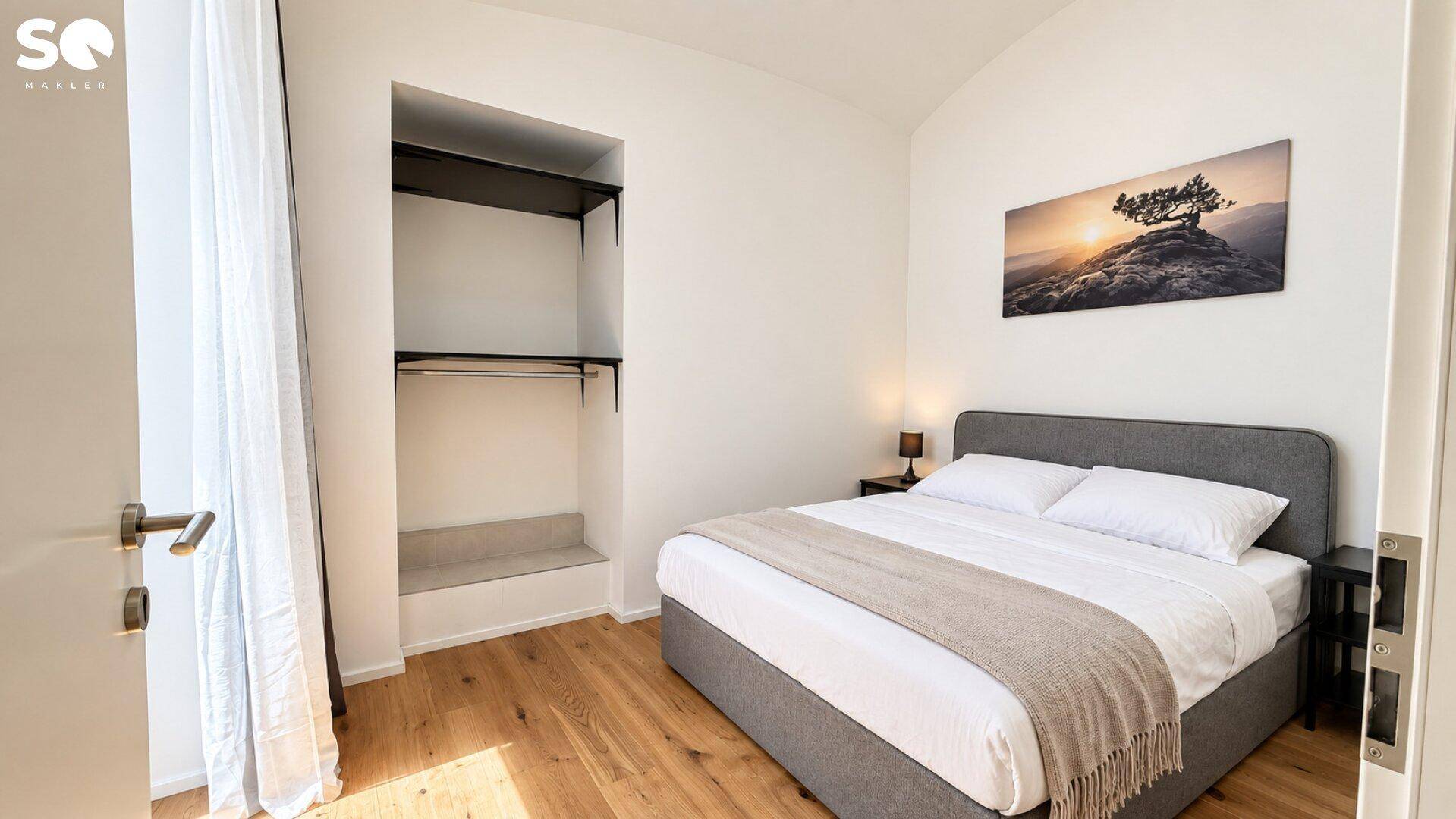 Helles Schlafzimmer mit Doppelbett, Holzboden und offener Nische für Kleiderschränke.