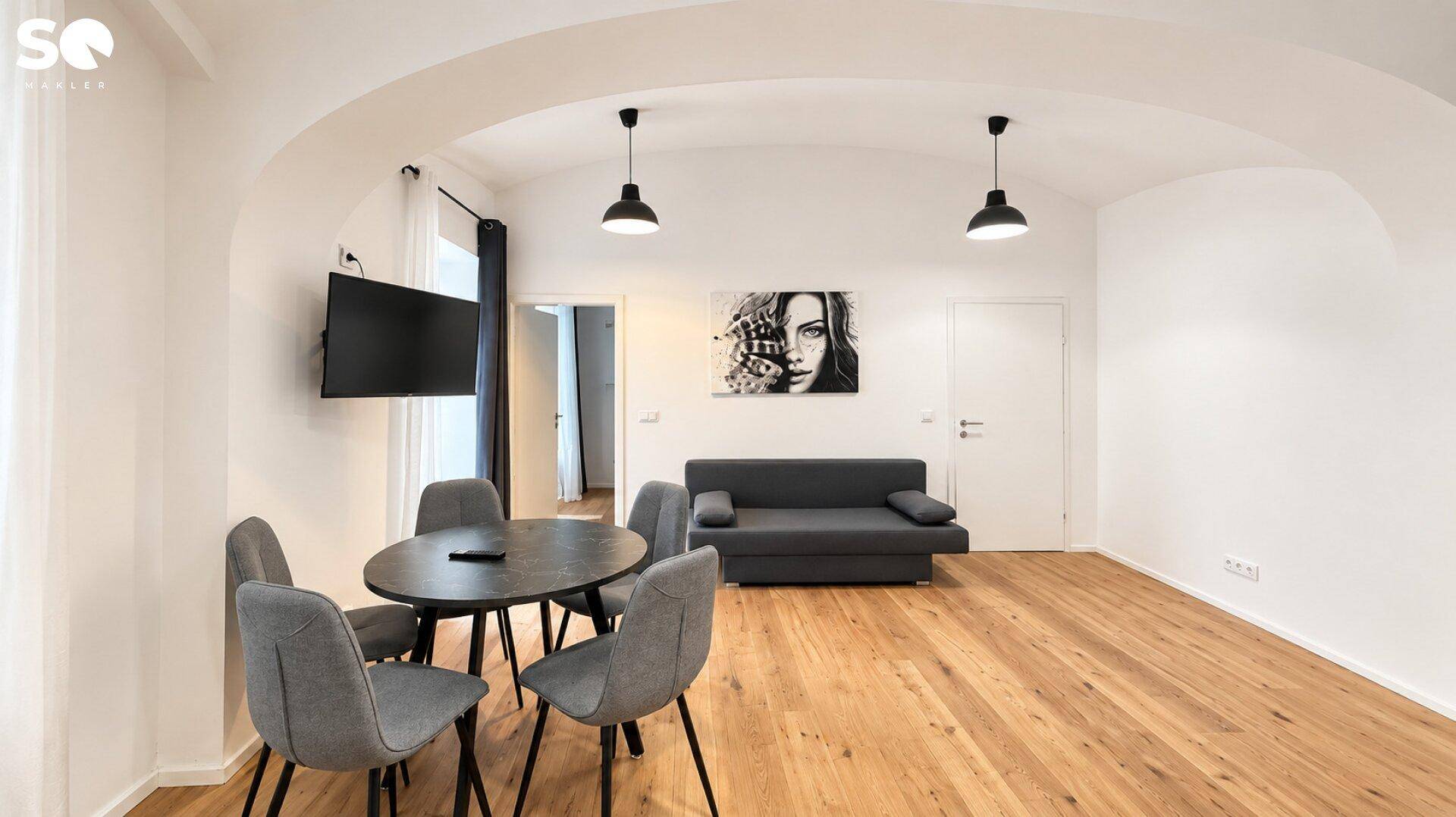 Gemütlicher Wohn- und Essbereich mit modernem Sofa, Esstisch und Fernseher an der Wand.