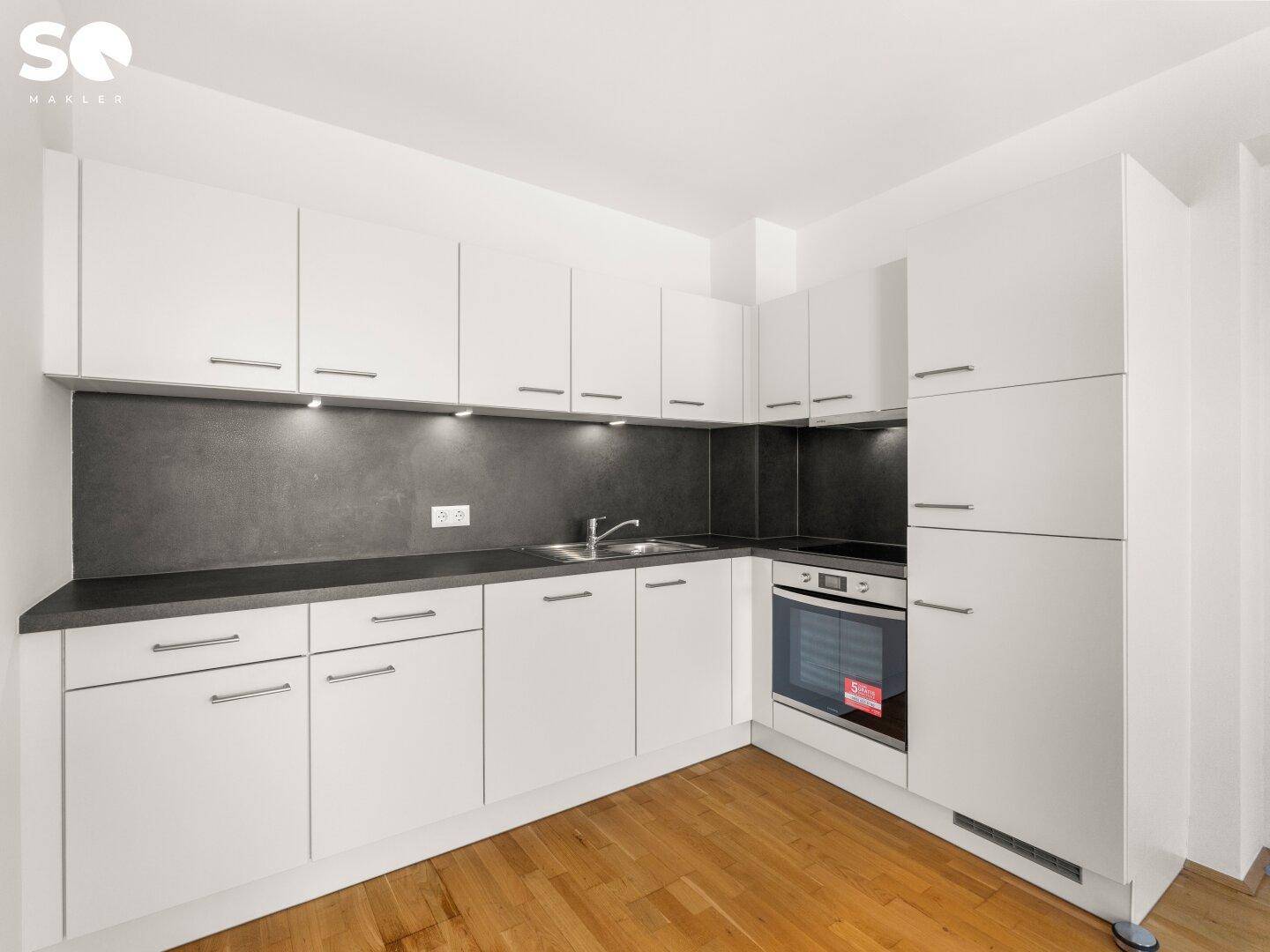 Moderne Einbauküche mit weißen Schränken, dunkler Arbeitsplatte und integrierten Geräten.