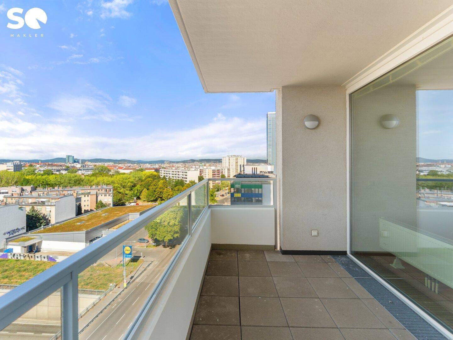 Geräumiger Balkon mit Glasgeländer und weitem Blick über die Stadtlandschaft.