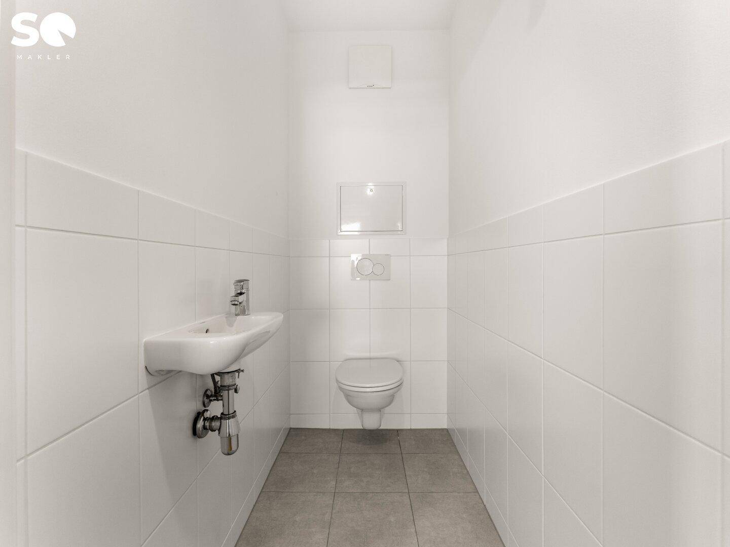Separates Gäste-WC mit weißen Fliesen, wandhängender Toilette und kleinem Waschbecken.