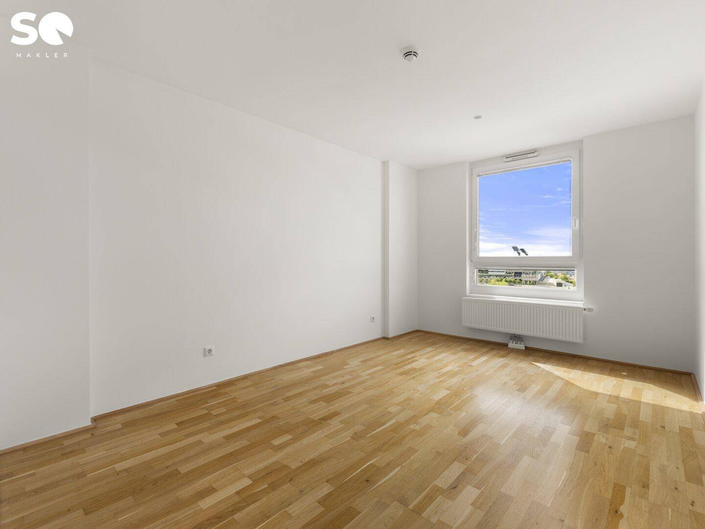 Leeres Zimmer mit hellem Parkettboden und großem Fenster, ideal als Schlafzimmer.