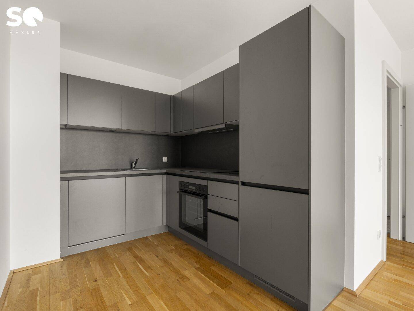 Moderne Einbauküche in Grau mit integrierten Geräten und Holzparkettboden.