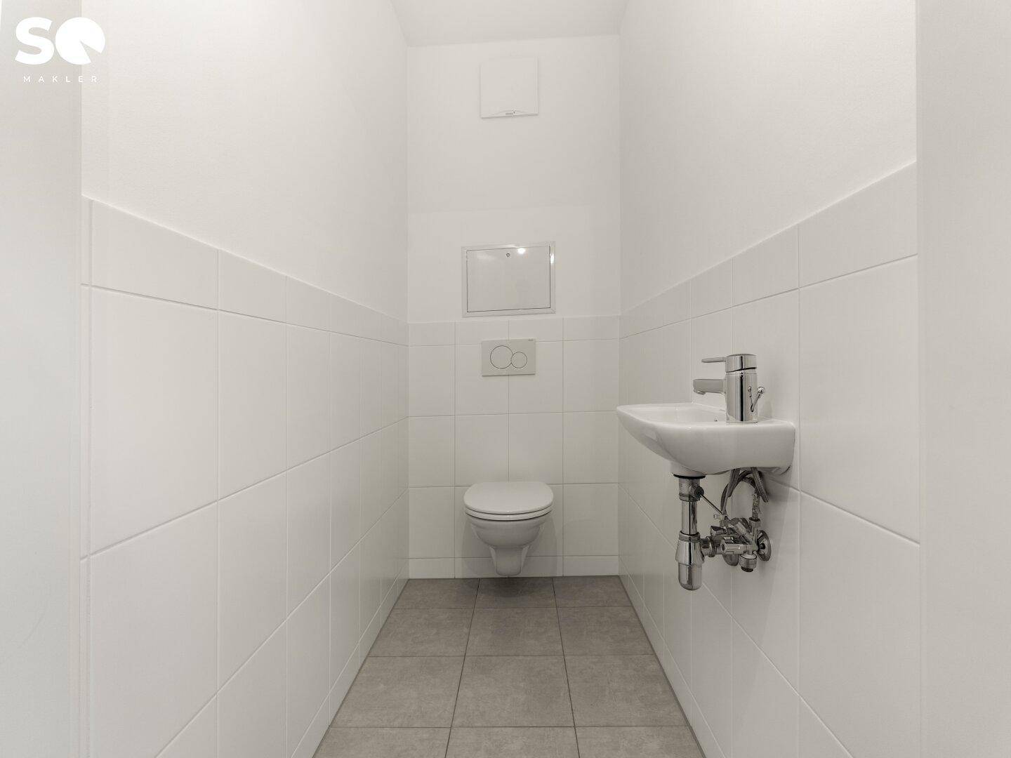 Separates WC mit Wand-WC, kleinem Waschbecken und weißen Fliesen.
