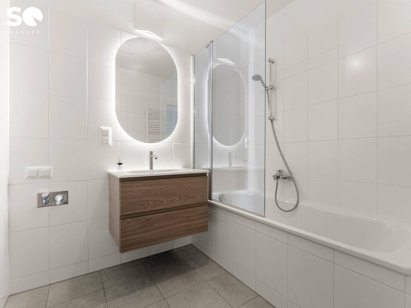 Modernes Badezimmer mit Badewanne, Duschabtrennung und beleuchtetem Spiegel.