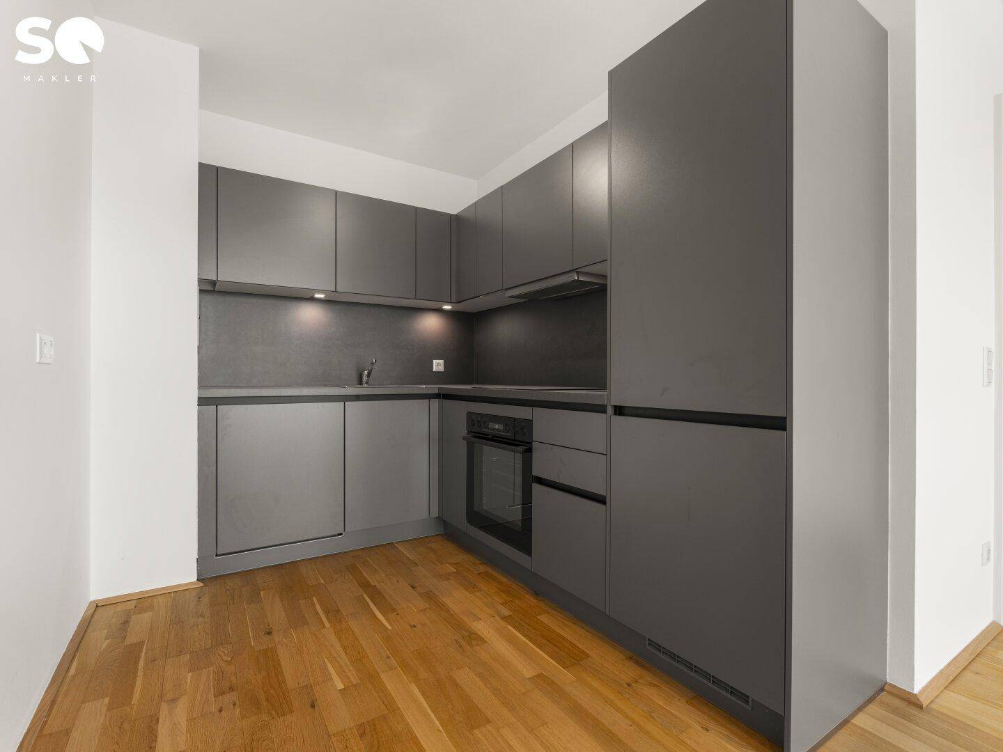 Kompakte, moderne Küche in Grau mit integriertem Backofen und Dunstabzugshaube.