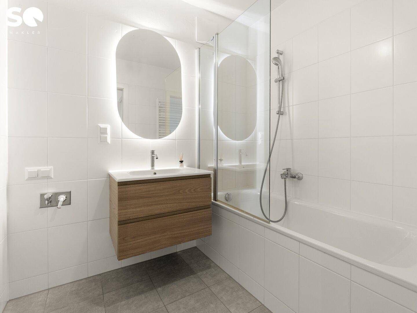 Modernes Badezimmer mit weißen Fliesen, schwebendem Waschtisch und Badewanne mit Duschwand.