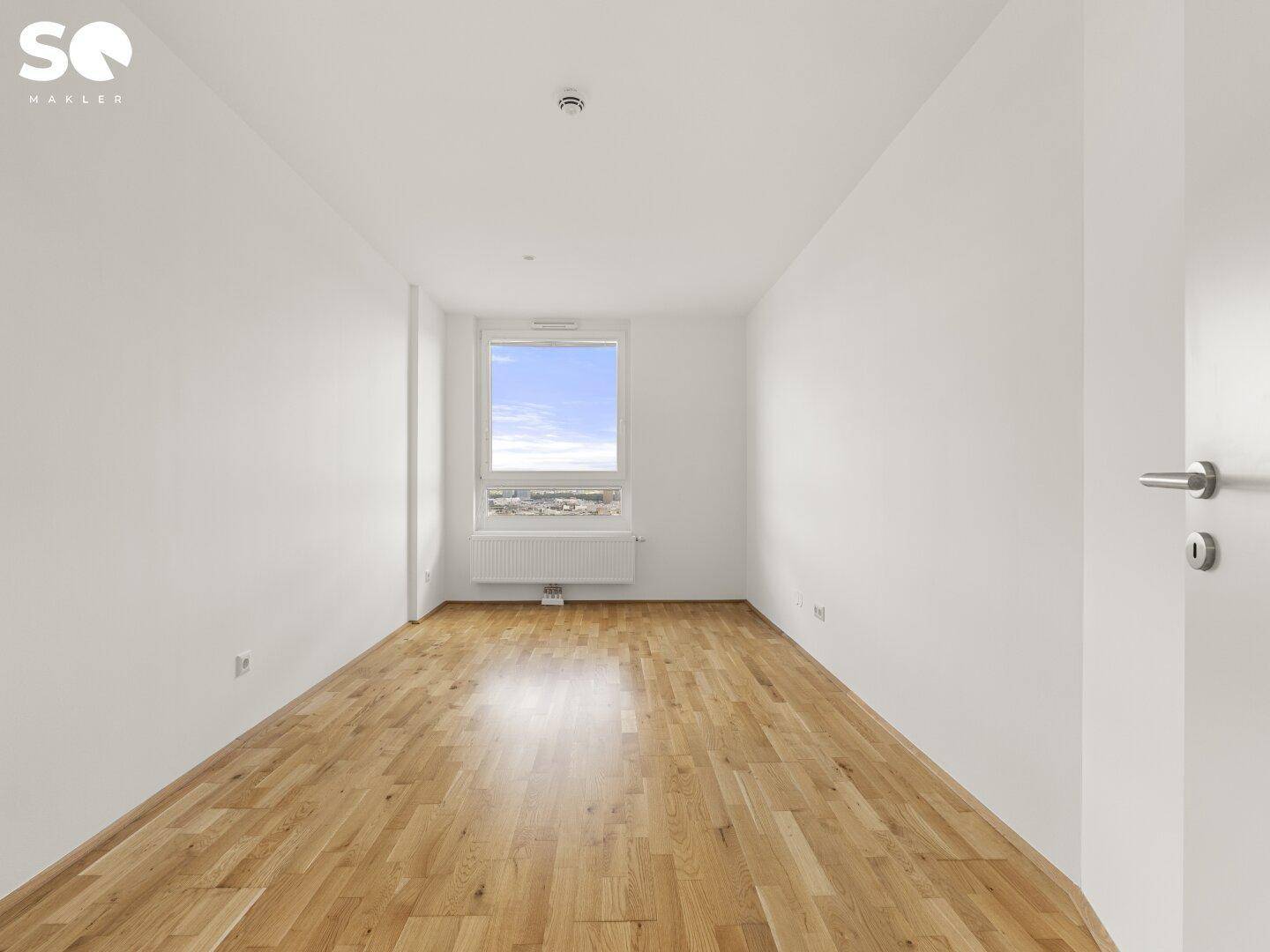 Leeres Schlafzimmer mit Parkettboden, weißen Wänden und einem Fenster.