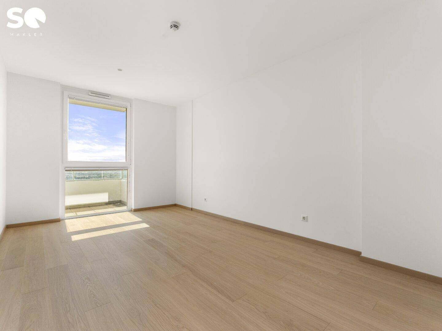 Helles Schlafzimmer mit Parkettboden und großem Fenster mit Zugang zum Balkon.