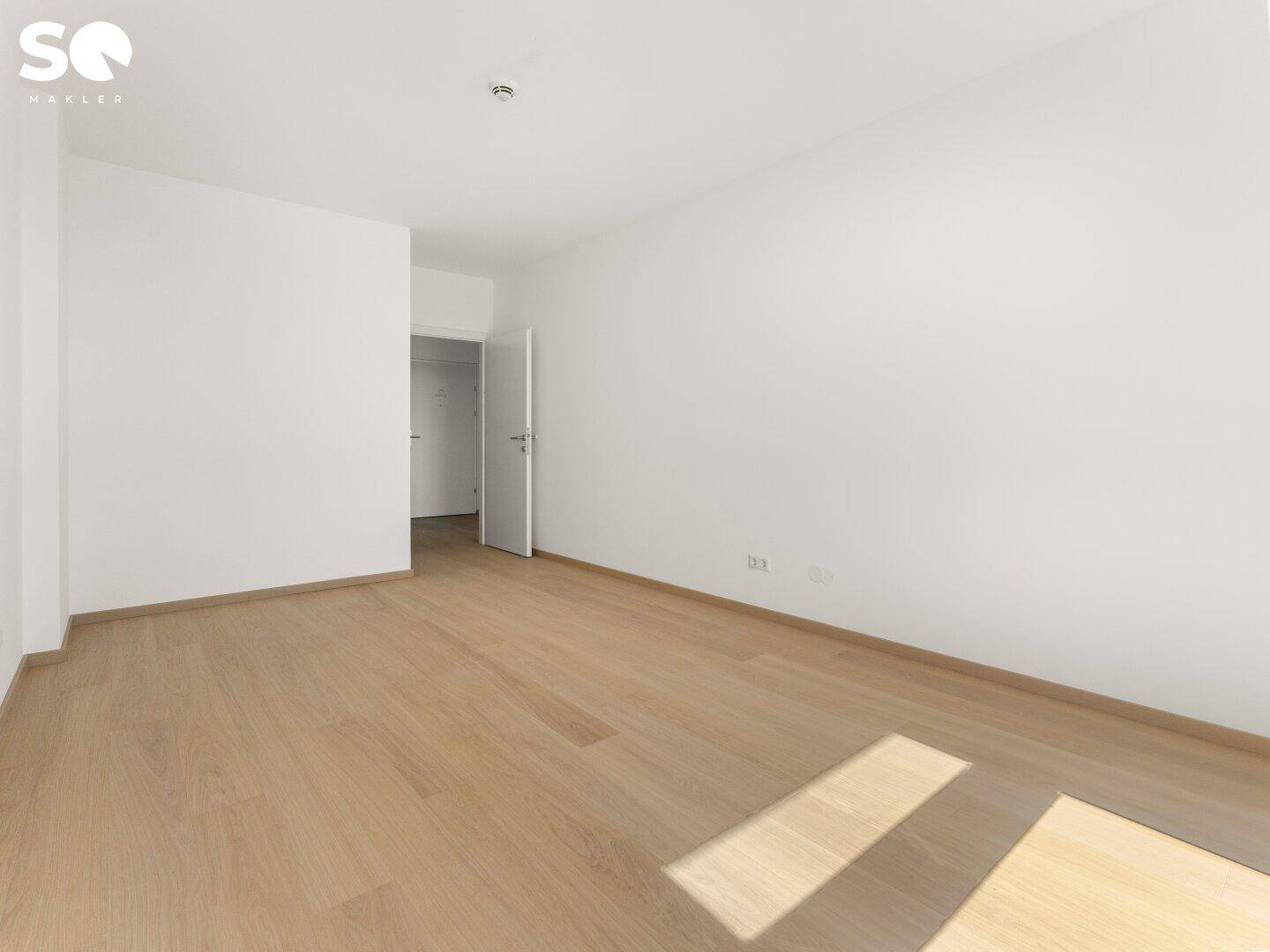 Leeres Zimmer mit hellem Parkettboden und weiß gestrichenen Wänden, bereit zum Einzug.