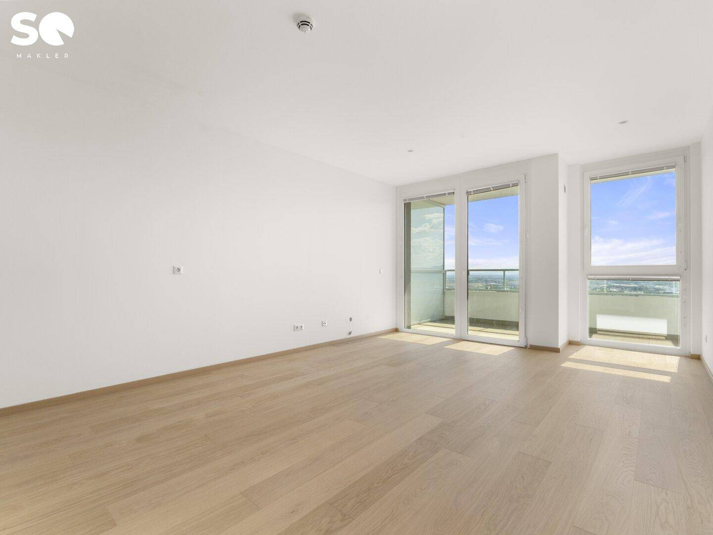 Helles, leeres Wohnzimmer mit hellem Parkettboden und Zugang zum Balkon.