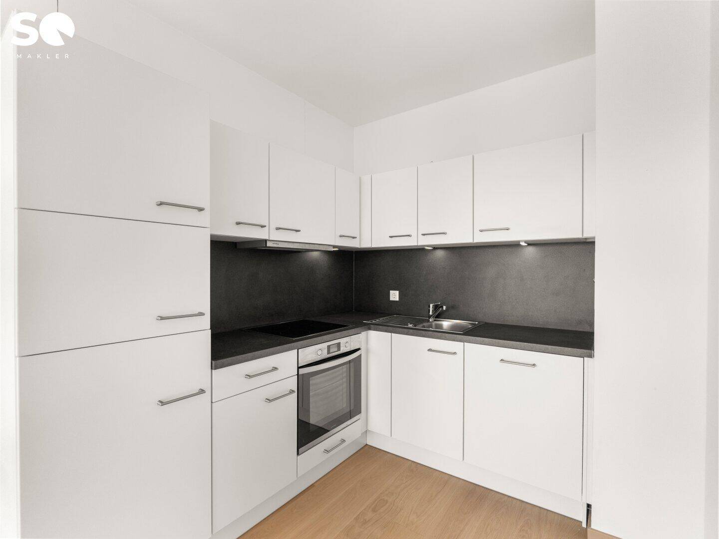 Moderne Einbauküche in Weiß mit dunkler Arbeitsplatte und integrierten Geräten.