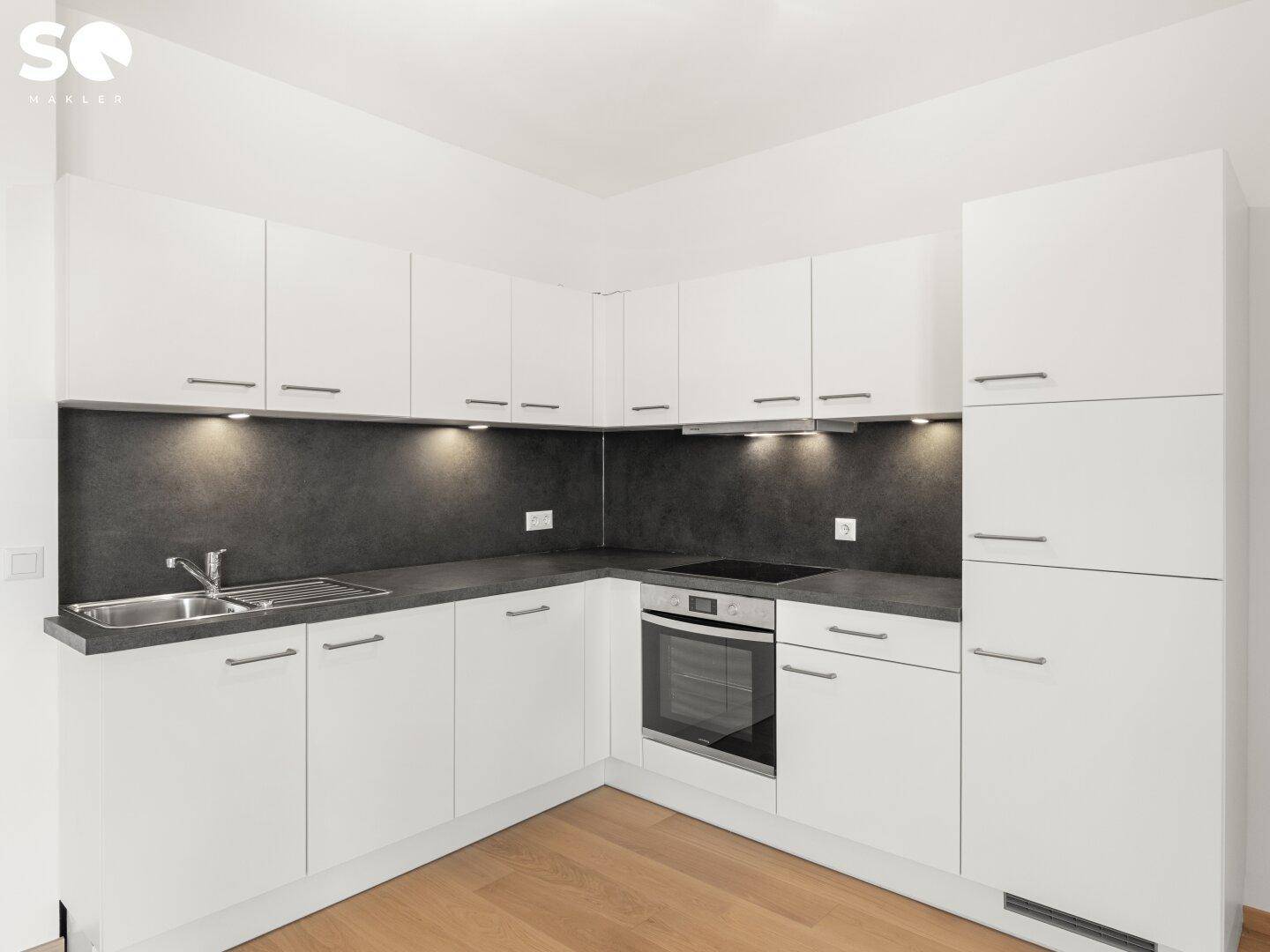Moderne weiße Einbauküche mit dunkler Arbeitsplatte, integriertem Backofen und Unterbauleuchten.