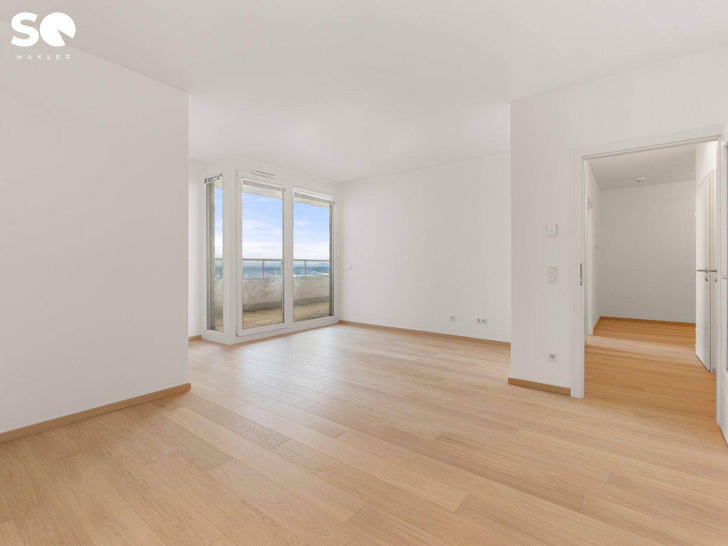 Heller, leerer Wohnbereich mit großen Fenstern und Zugang zum Balkon, ausgestattet mit Parkettboden.