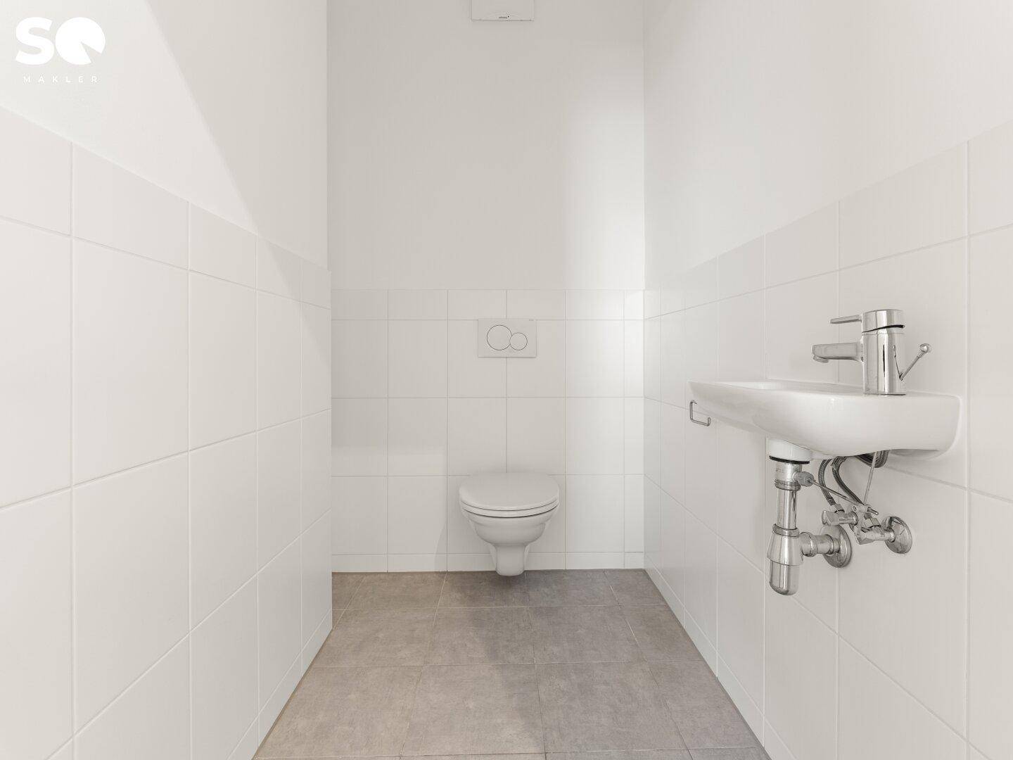 Sauberes Gäste-WC mit weißen Wandfliesen, wandhängender Toilette und kleinem Waschbecken.