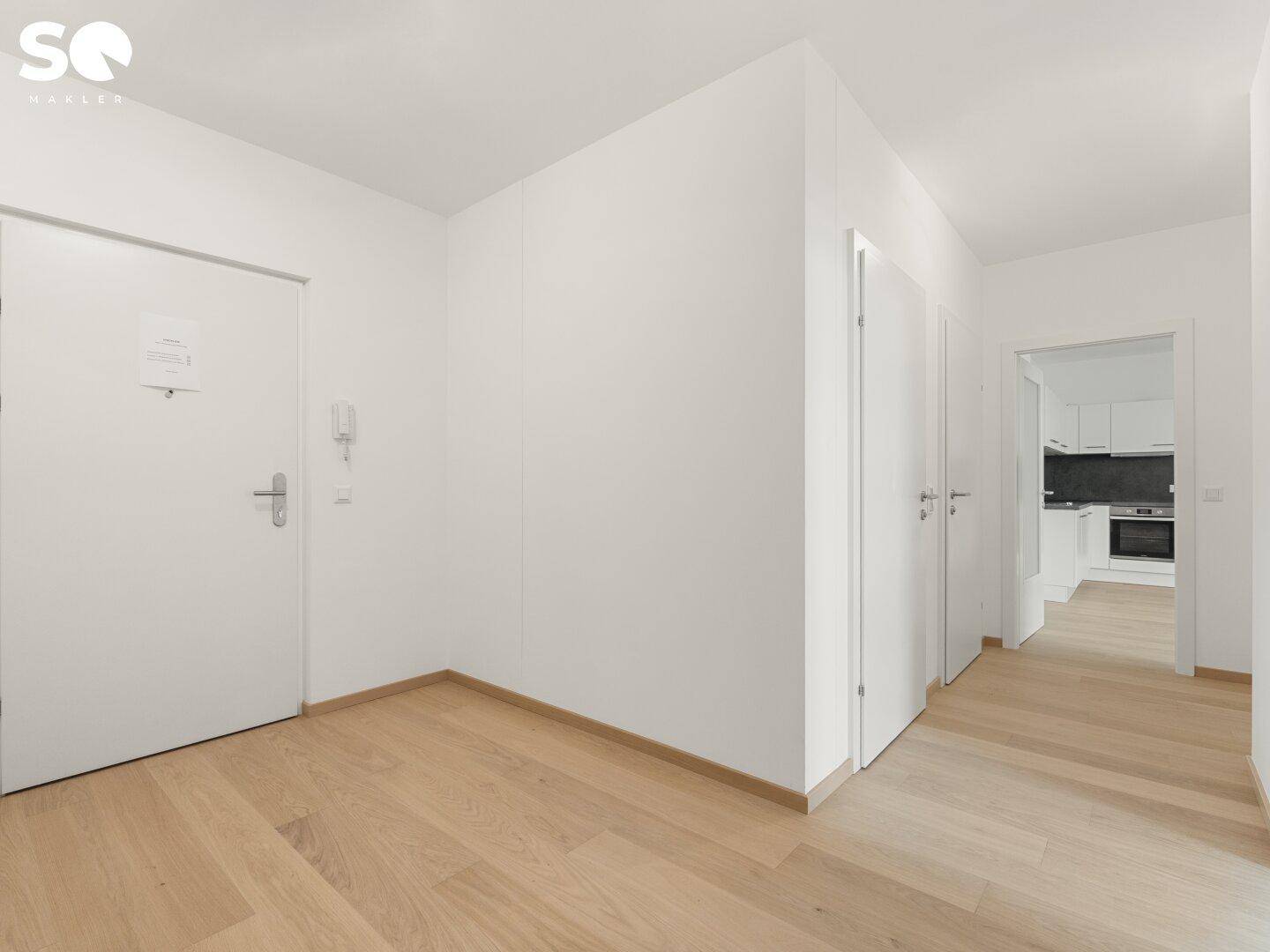 Heller Eingangsbereich mit Holzboden und weißen Türen, der zu weiteren Räumen führt.