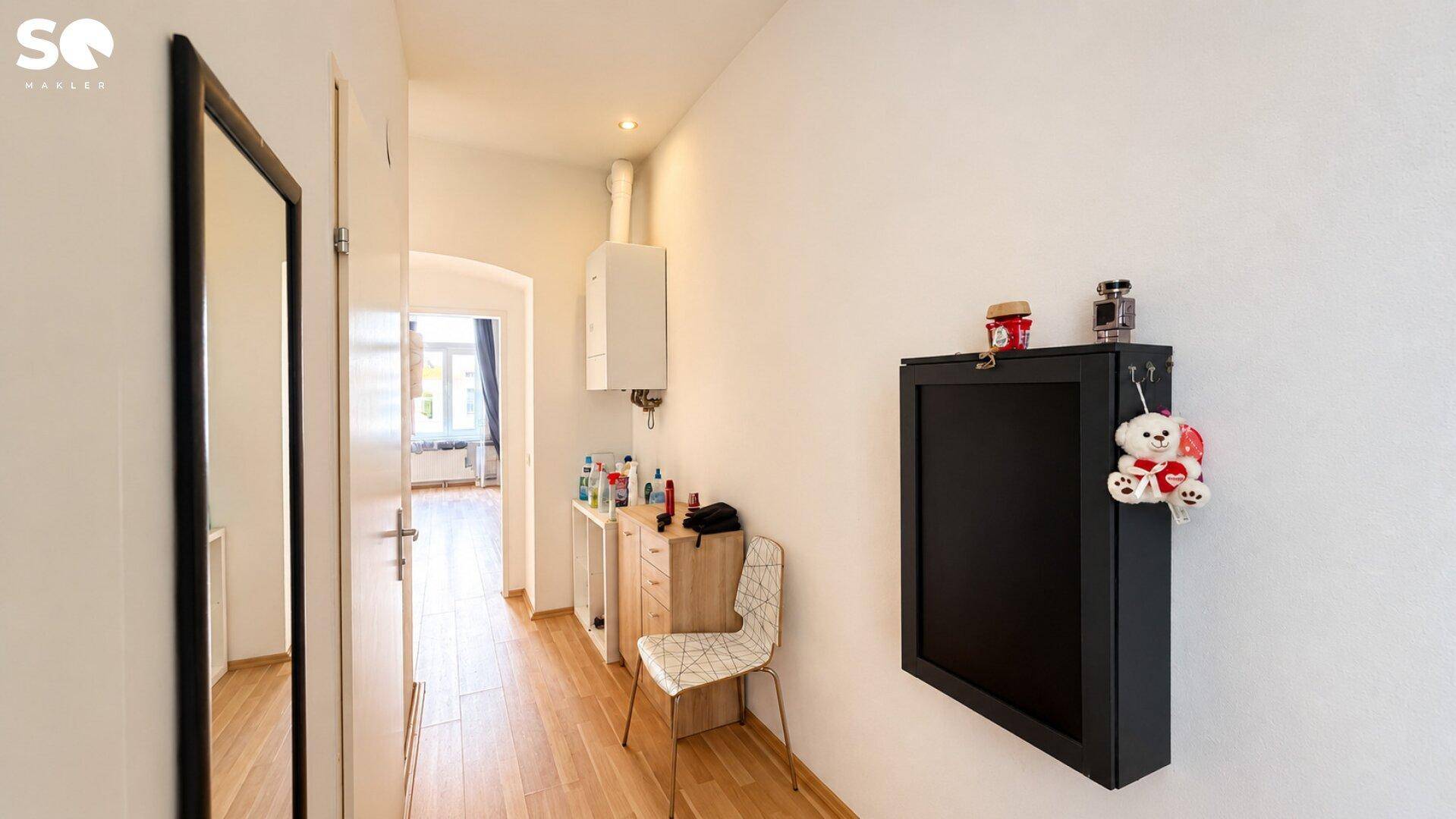 Schmaler Flur mit Holzfußboden, Spiegel und moderner Wanddekoration.