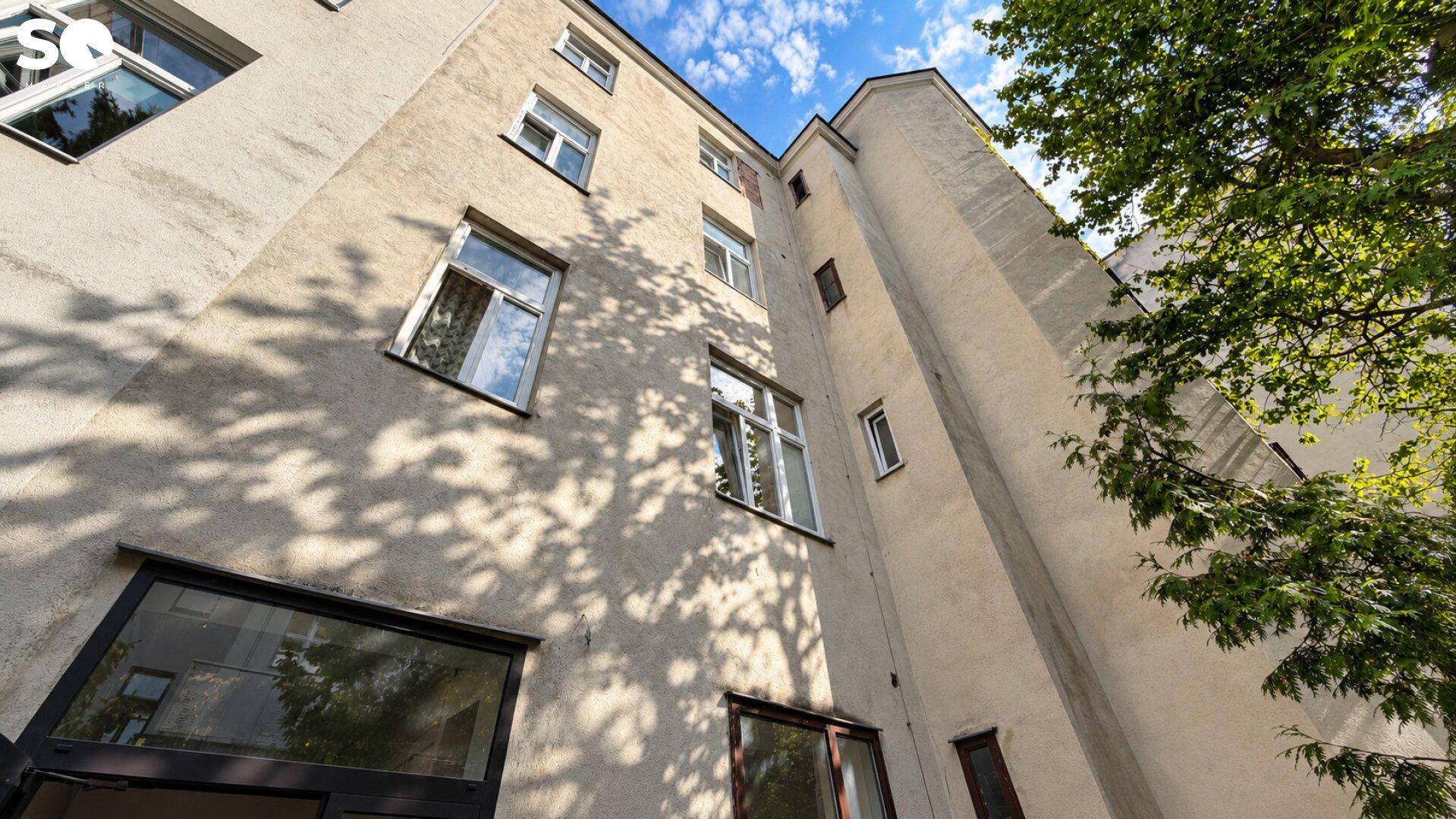 Rückseite eines Mehrfamilienhauses mit schlichter Fassade und Bäumen im Innenhof.