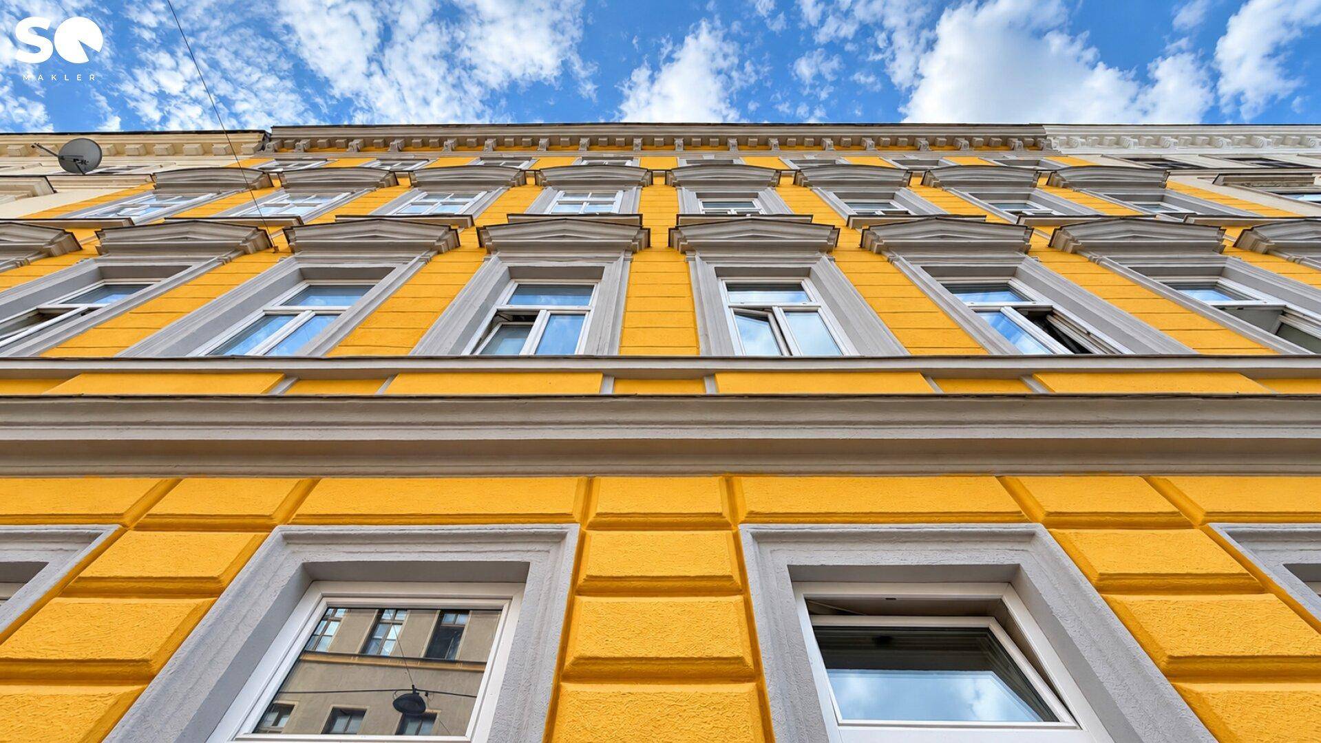 Detailansicht der gelben Fassade eines Altbaus mit vielen Fenstern und Stuckelementen.