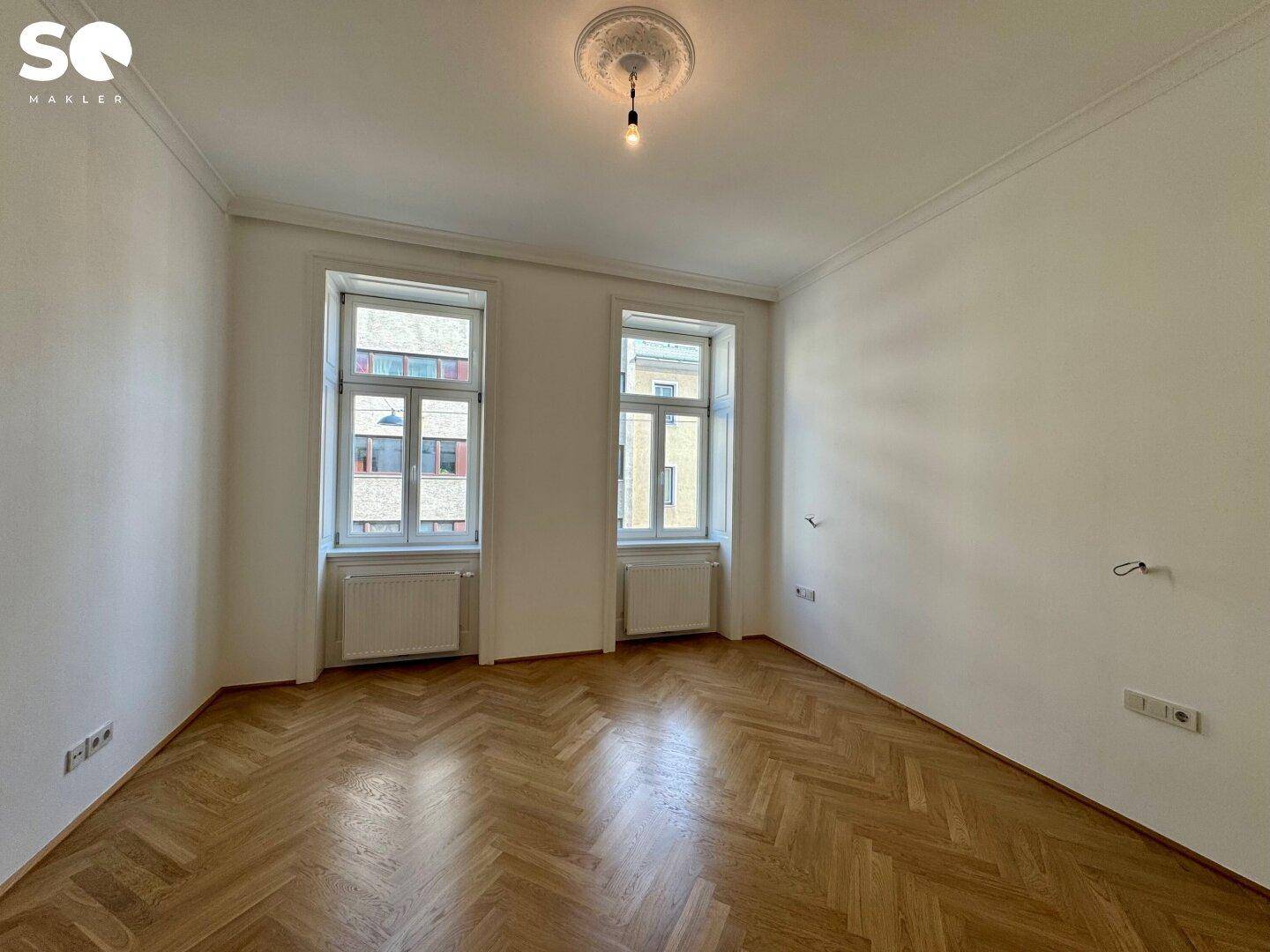 Lichtdurchflutetes Zimmer mit elegantem Fischgrätparkett und Blick auf die umliegenden Gebäude.