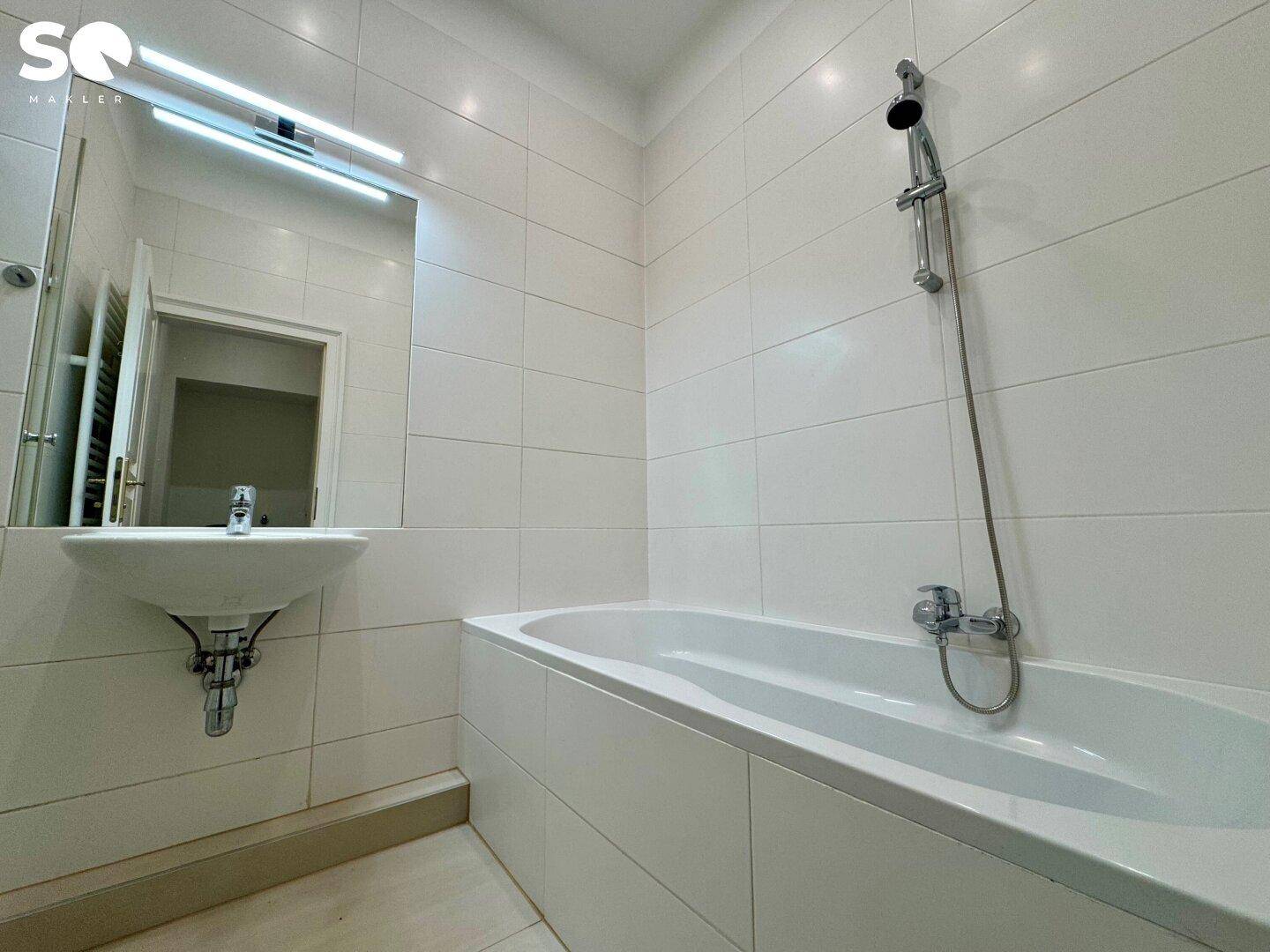 Helles Badezimmer mit Badewanne, Waschbecken und weißen Wandfliesen.