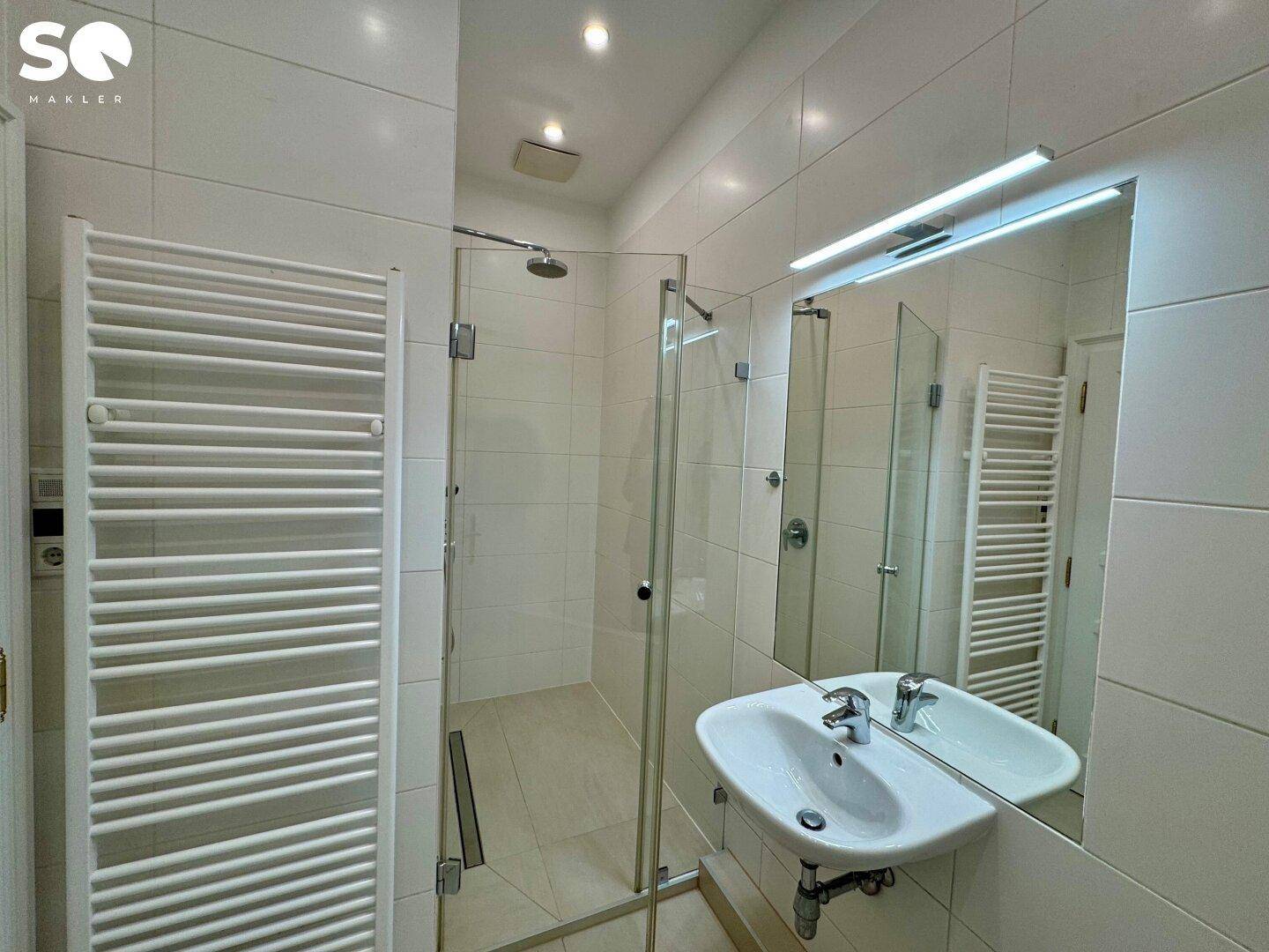 Modernes Badezimmer mit begehbarer Dusche, weißen Fliesen und beheiztem Handtuchhalter.