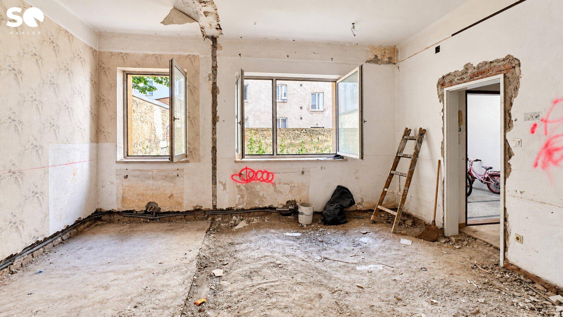 Renovierungsbedürftiger Raum mit zwei geöffneten Fenstern, Betonboden und Blick auf den Innenhof.