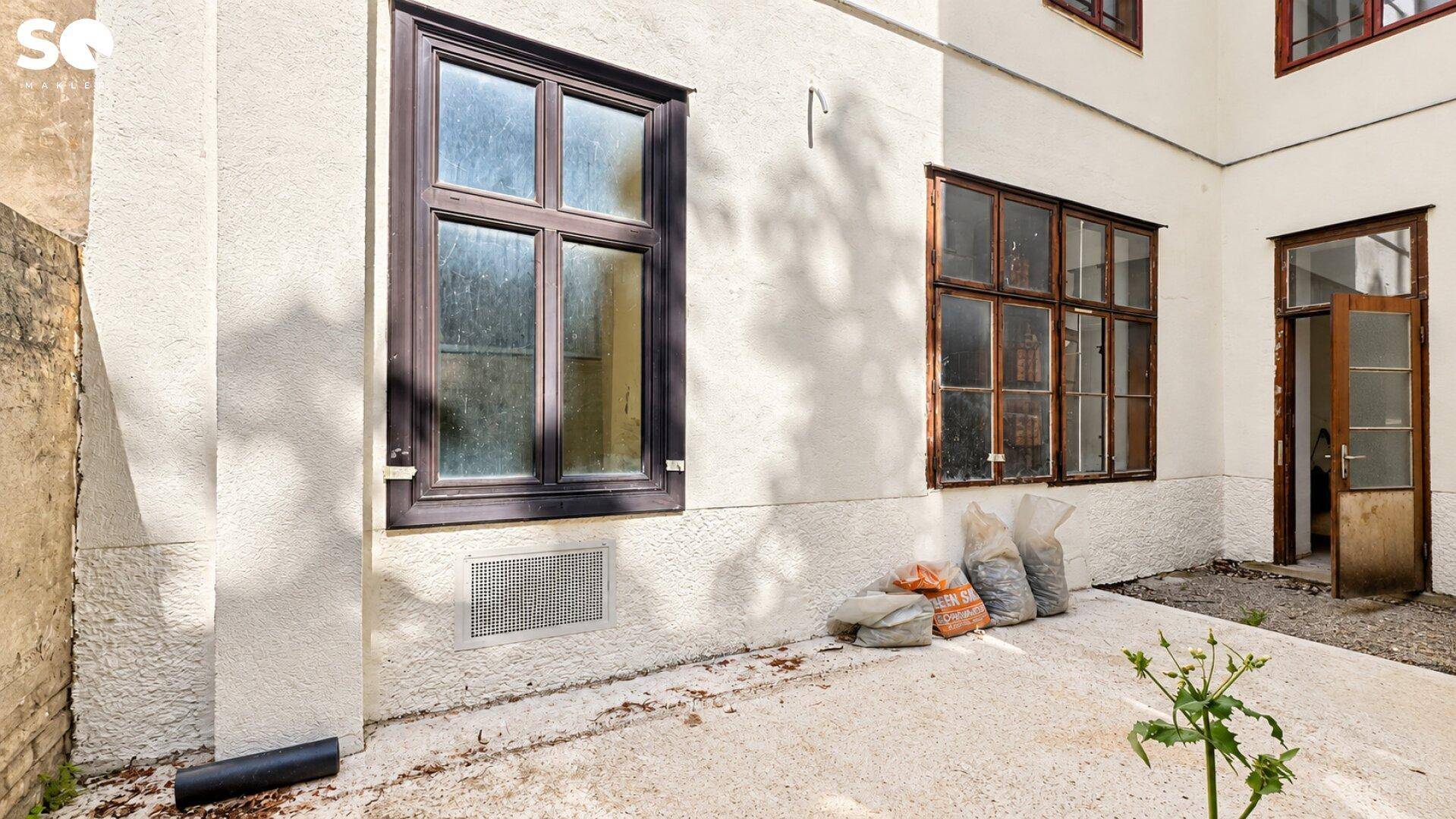 Kleiner gepflasterter Außenbereich mit Fenstern und einer Tür, bereit für die Gestaltung.