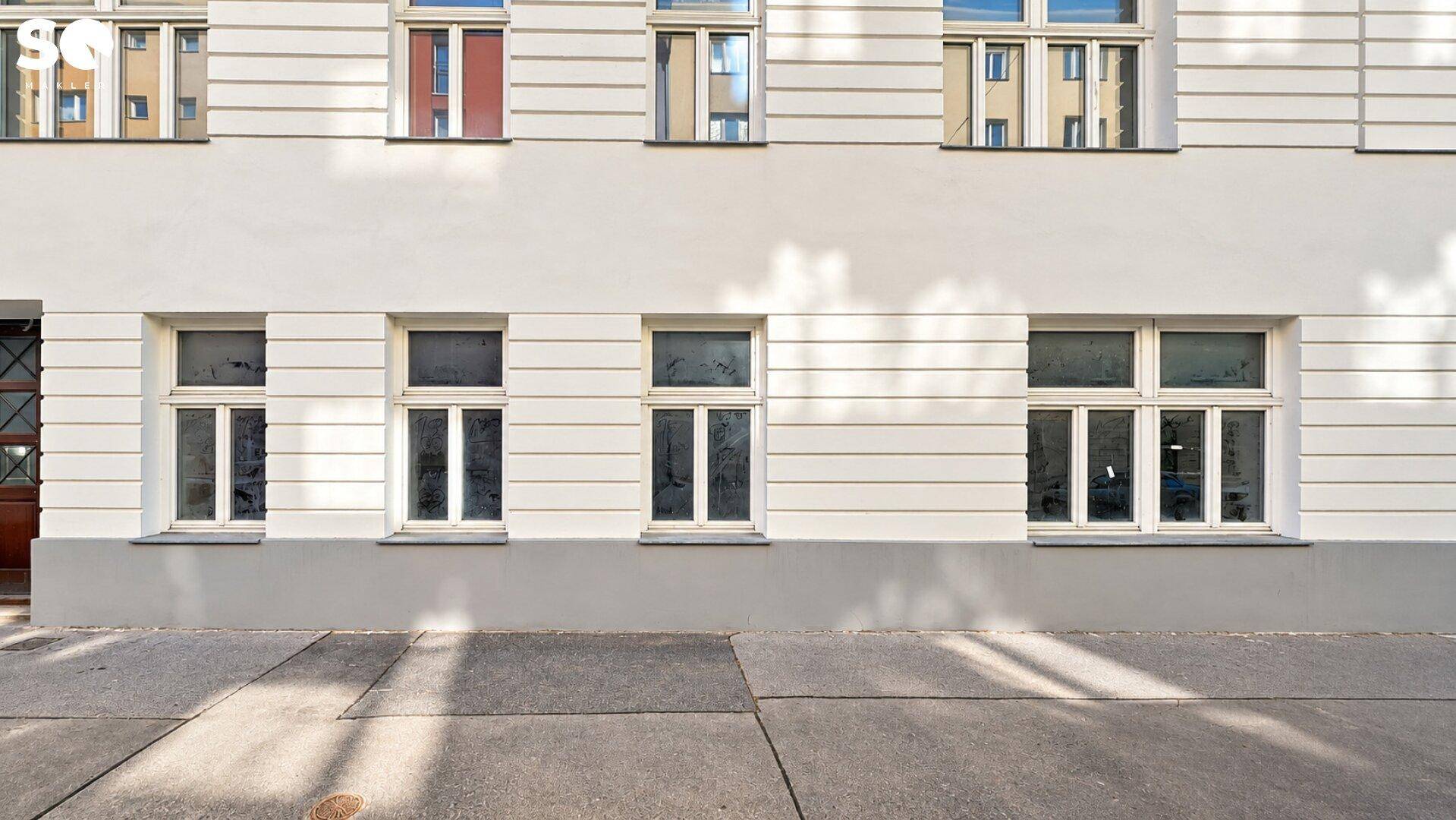 Weiße Gebäudefassade mit mehreren Fenstern und einem Bürgersteig im Vordergrund.