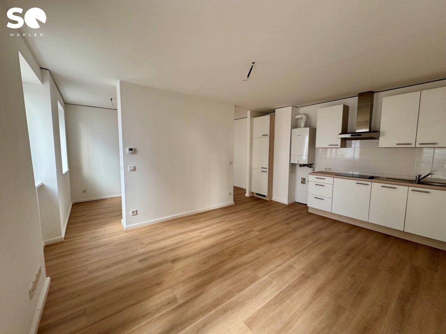 Moderner Wohnbereich mit integrierter weißer Küchenzeile, Laminatboden und viel Tageslicht.