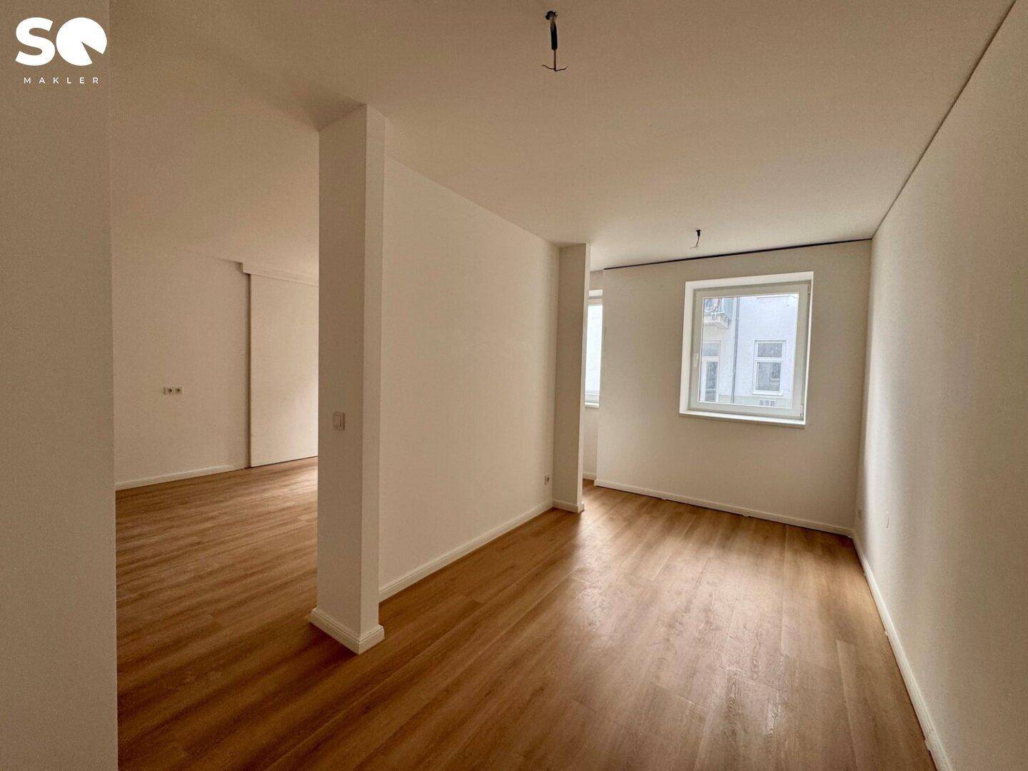 Heller Wohnraum mit Laminatboden und einem Fenster, das Tageslicht hereinlässt.