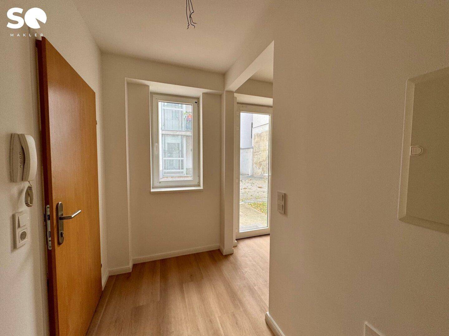 Eingangsbereich mit Holztür, Fenster und Zugang zu einem Außenbereich.