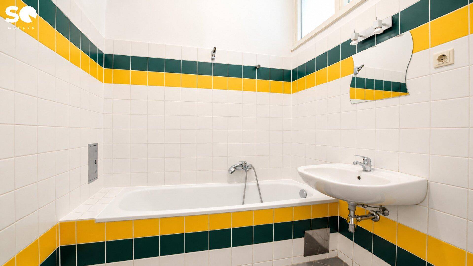 Badezimmer mit Badewanne, Waschbecken und auffälligen gelb-grünen Streifenfliesen an den Wänden.
