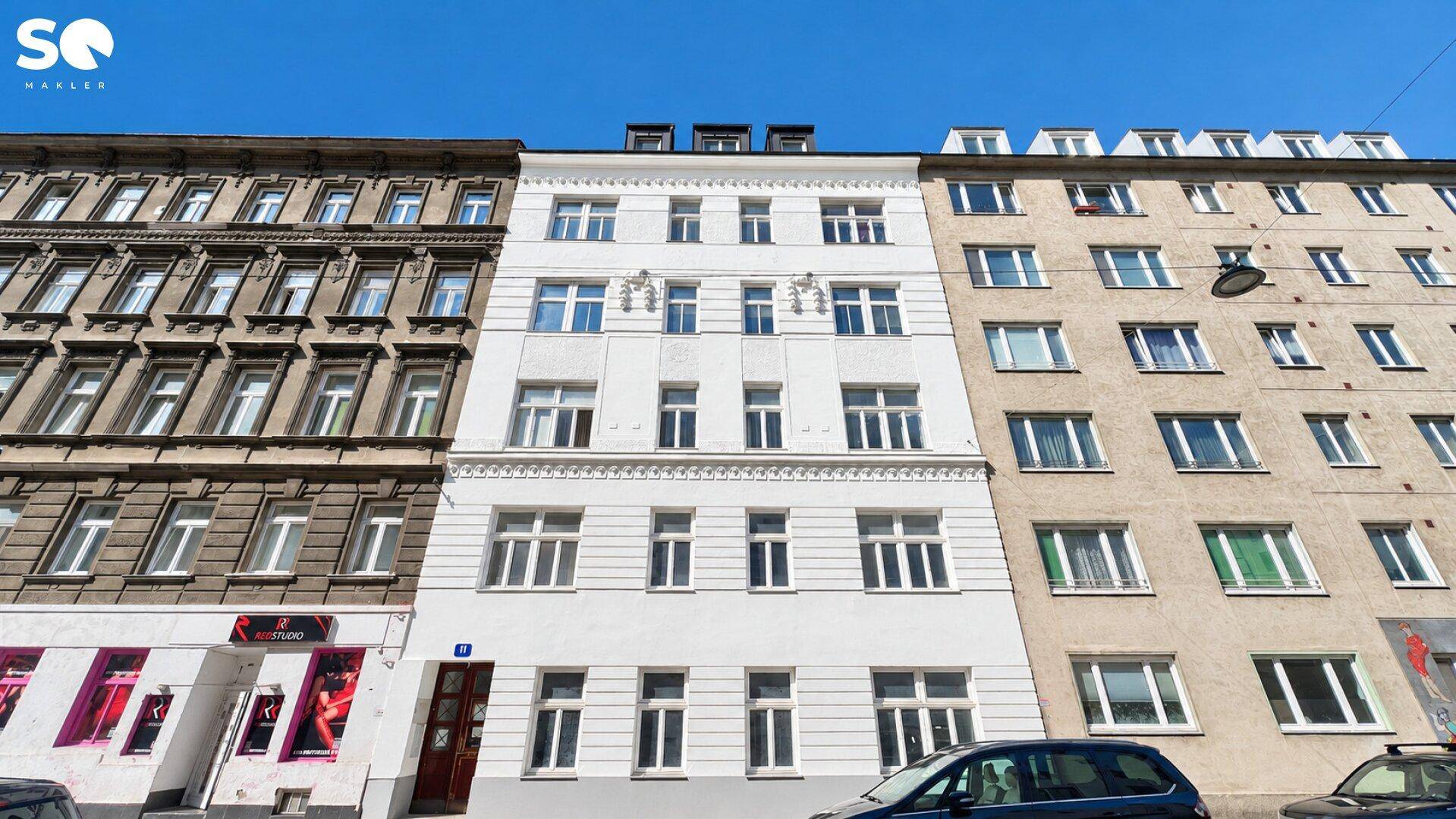 Gesamtansicht eines sanierten Mehrfamilienhauses mit angrenzenden Gebäuden unter klarem Himmel.