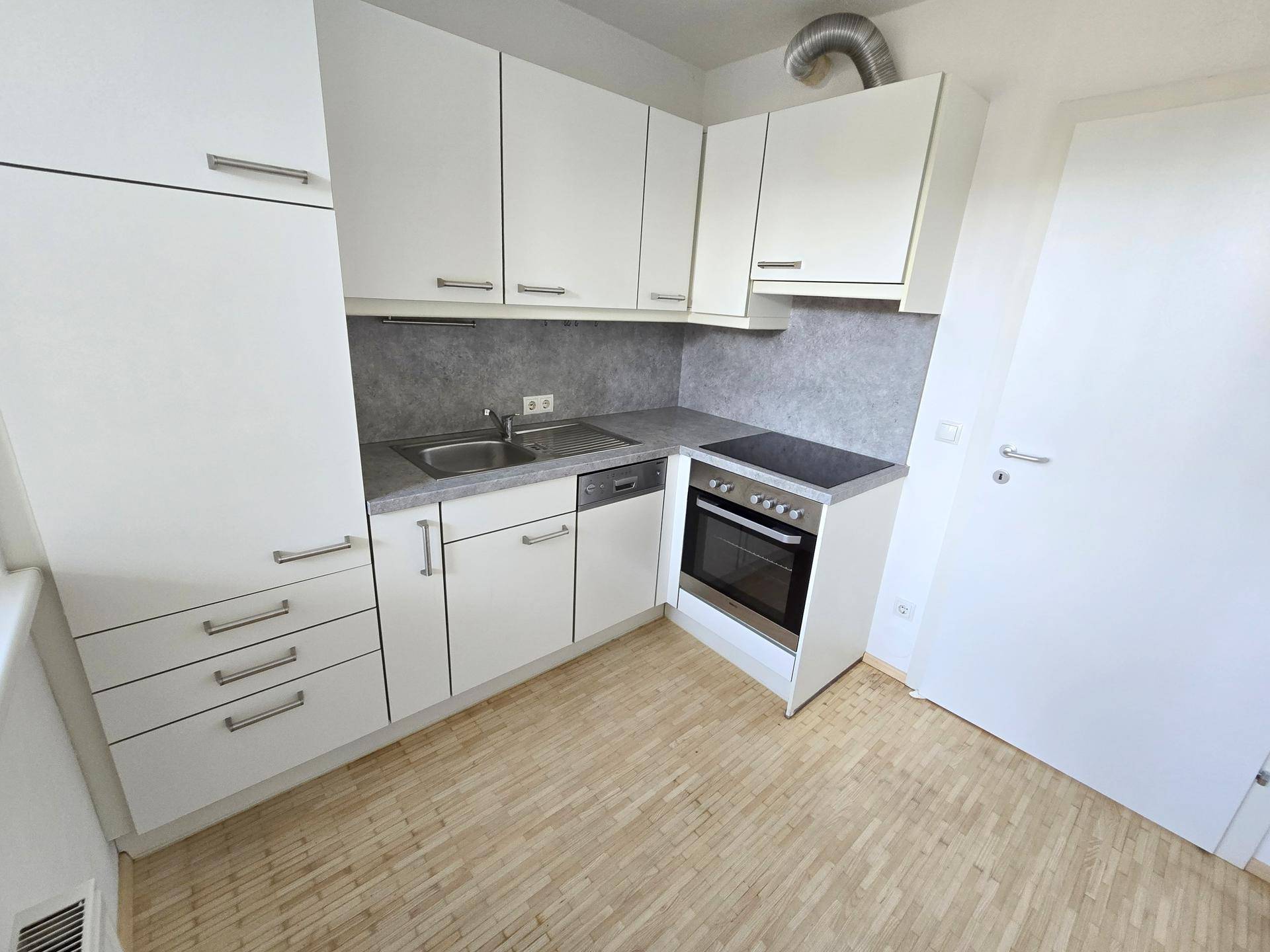 Kompakte, moderne Küche mit weißen Schränken, integriertem Backofen und Laminatboden.