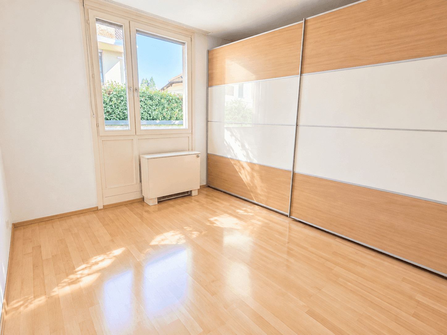 Helles Schlafzimmer mit Parkettboden und großem Einbauschrank, bietet viel Stauraum.