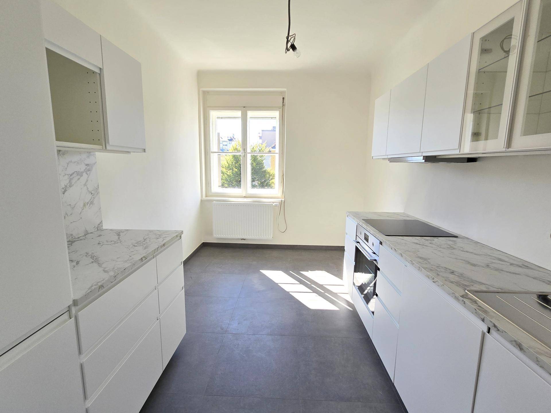 Moderne Küche mit weißen Schränken, Marmorarbeitsplatten und dunklem Fliesenboden.