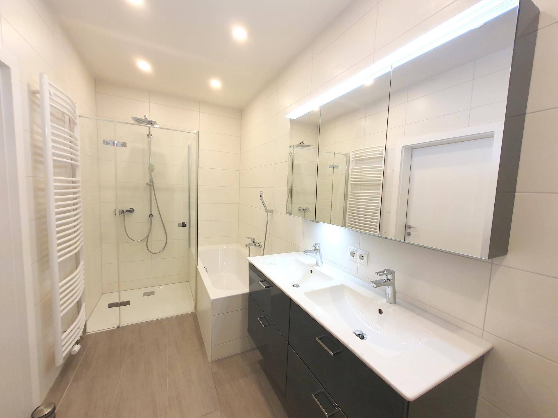 Modernes Badezimmer mit Doppelwaschbecken, Dusche und Badewanne, hell gefliest.