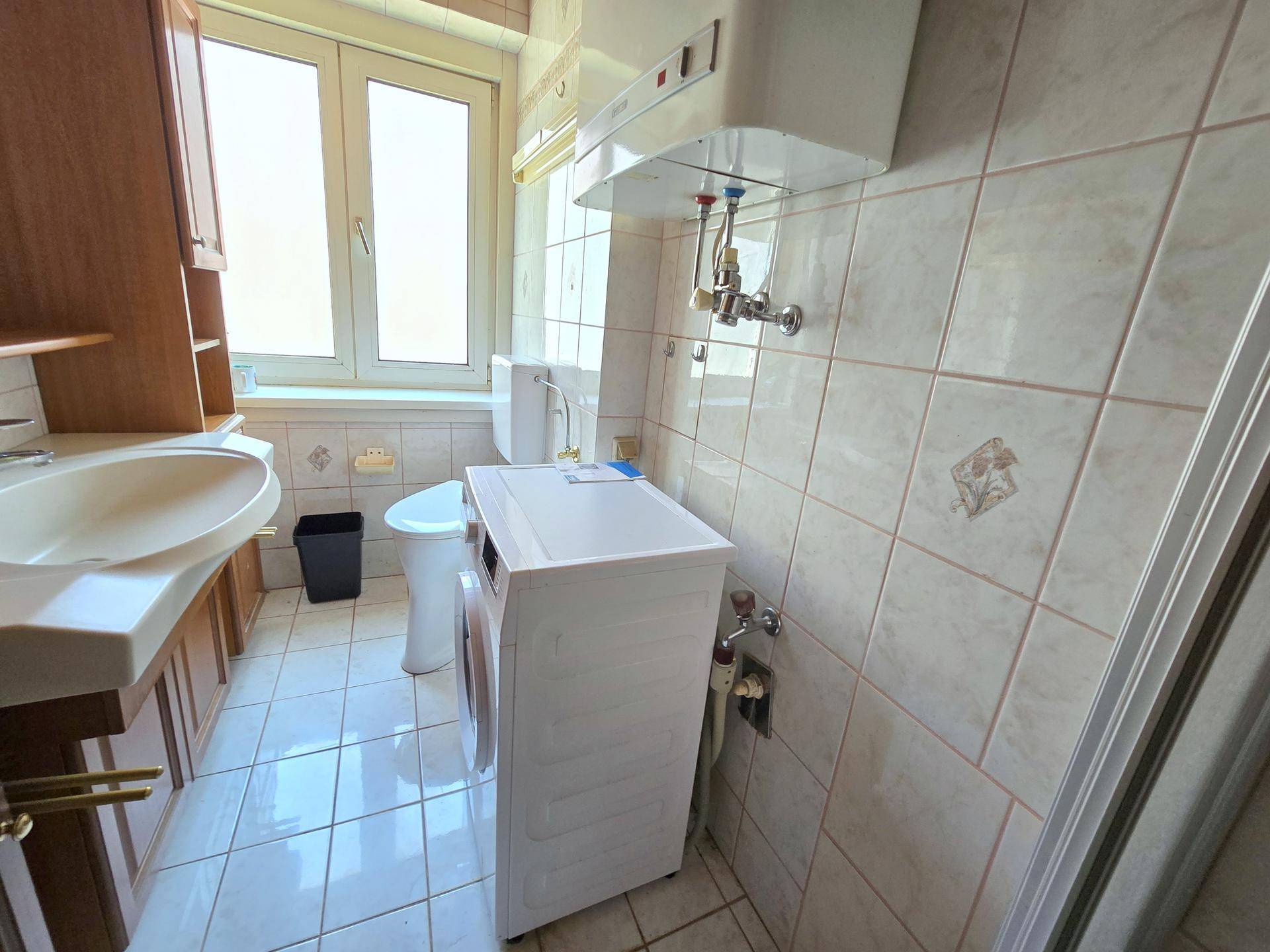 Gefliestes Badezimmer mit Fenster, Waschbecken, Toilette und Duschbereich.