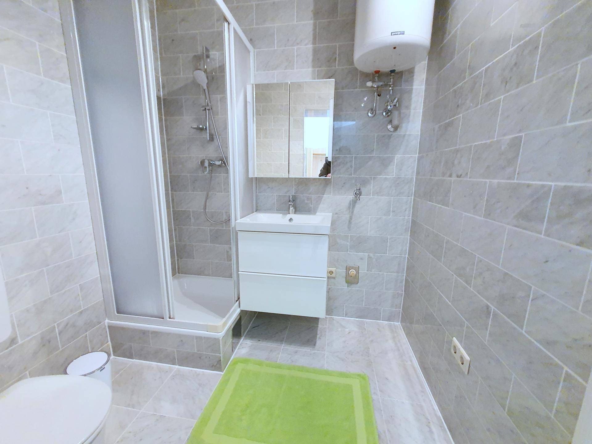 Modern gefliestes Badezimmer mit Duschkabine, Waschbecken und Spiegelschrank.
