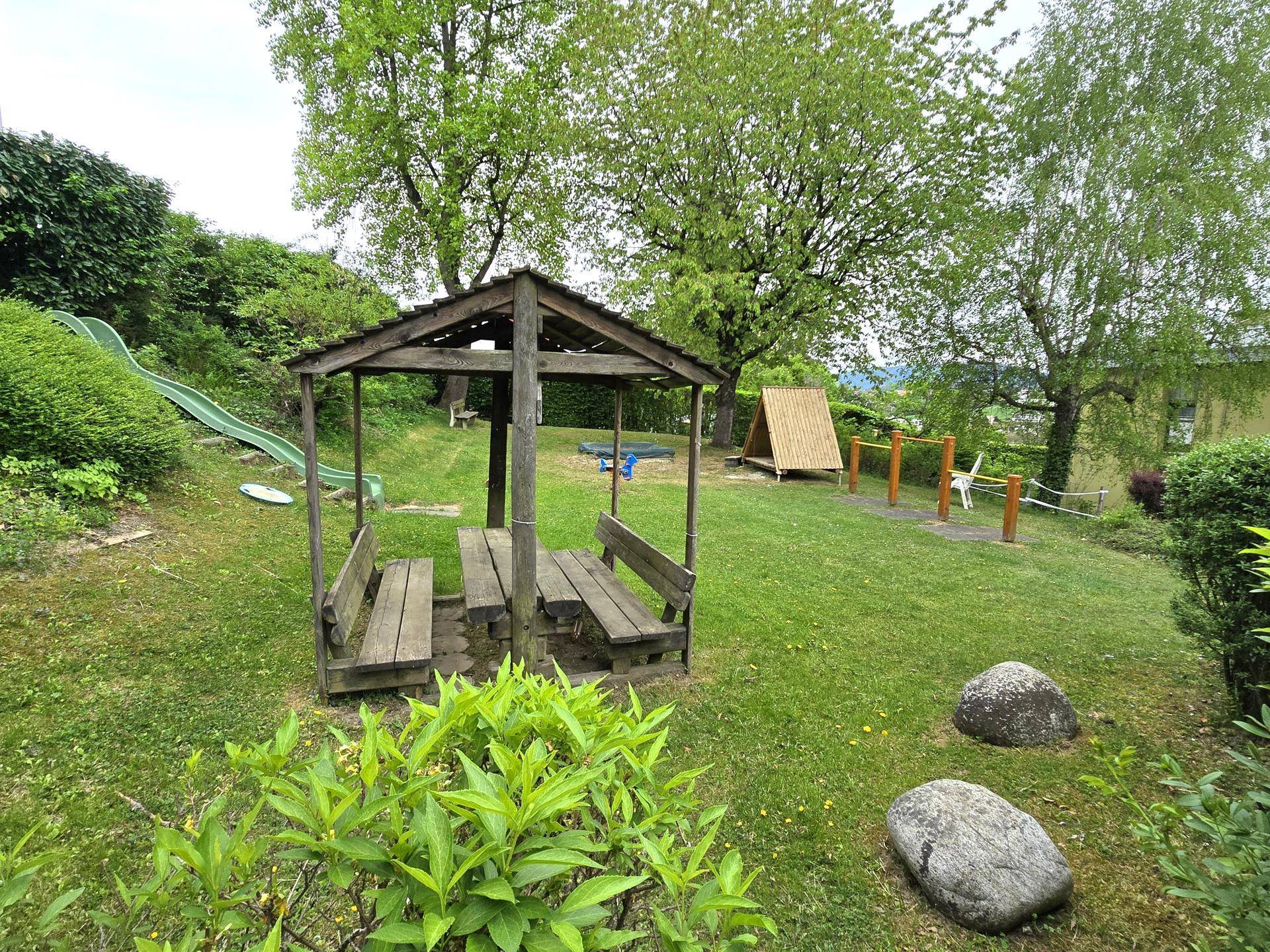 Weitläufiger Gartenbereich mit Spielgeräten, Rutsche und einem gemütlichen Holzpavillon, umgeben von viel Grün.