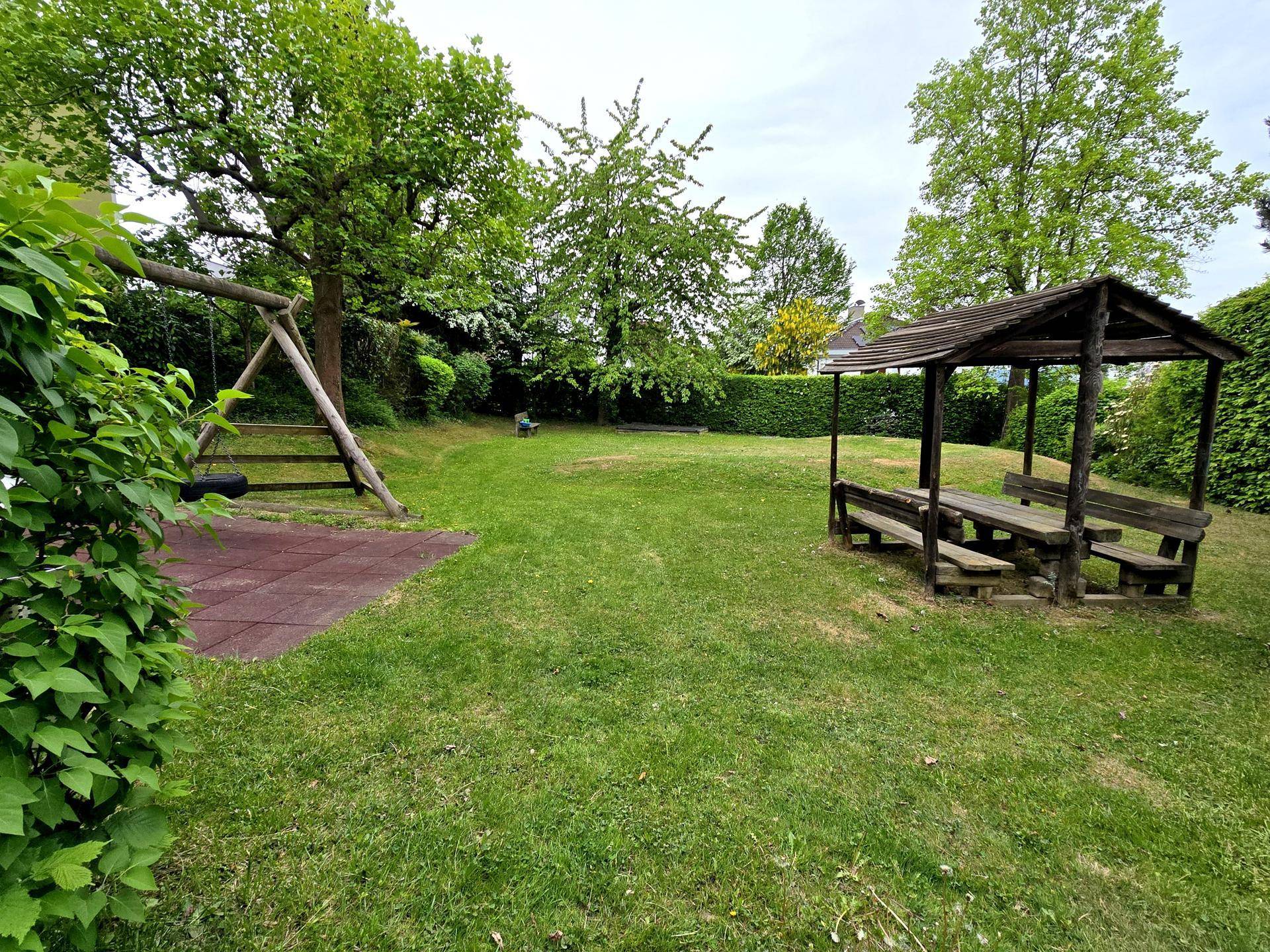 Großer Gemeinschaftsgarten mit Schaukel, Spielbereich und einem Holzpavillon für gesellige Stunden.
