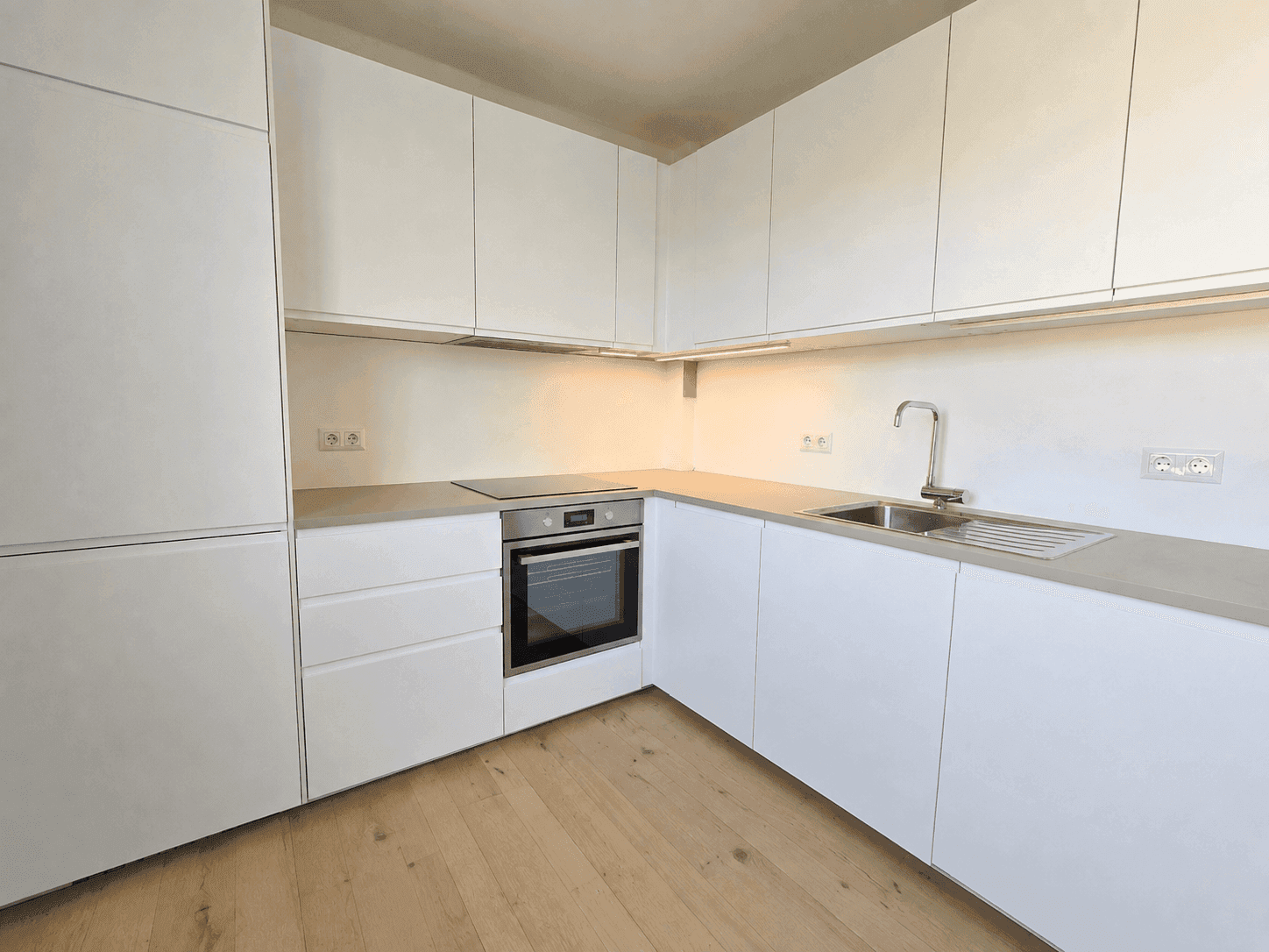 Moderne, helle Einbauküche mit weißen Schränken, integrierten Geräten und Holzfußboden.