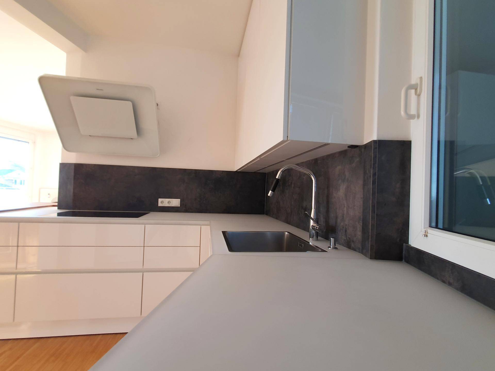 Moderne Küche mit weißen Hochglanzfronten, dunkler Arbeitsplatte und integrierter Spüle.