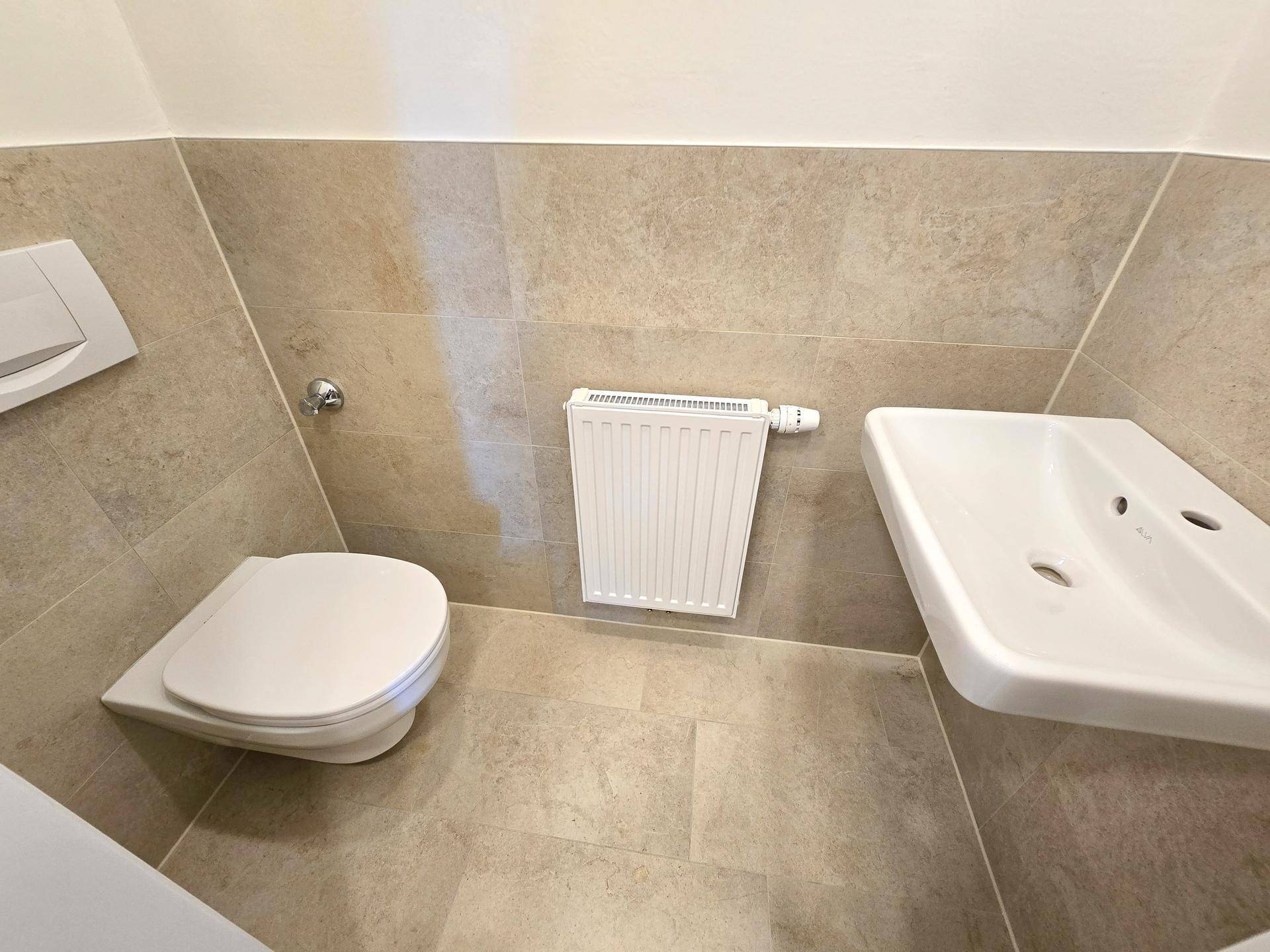 Kleines Gäste-WC mit Wand-WC, Waschbecken und hellen Fliesen.