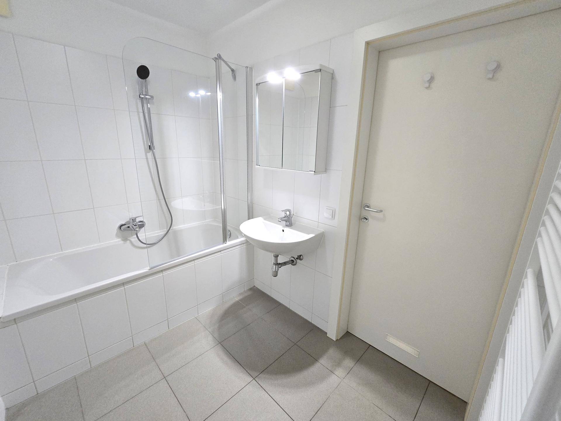Funktionales Badezimmer mit Badewanne, Duschwand, Einzelwaschbecken und beheiztem Handtuchhalter.